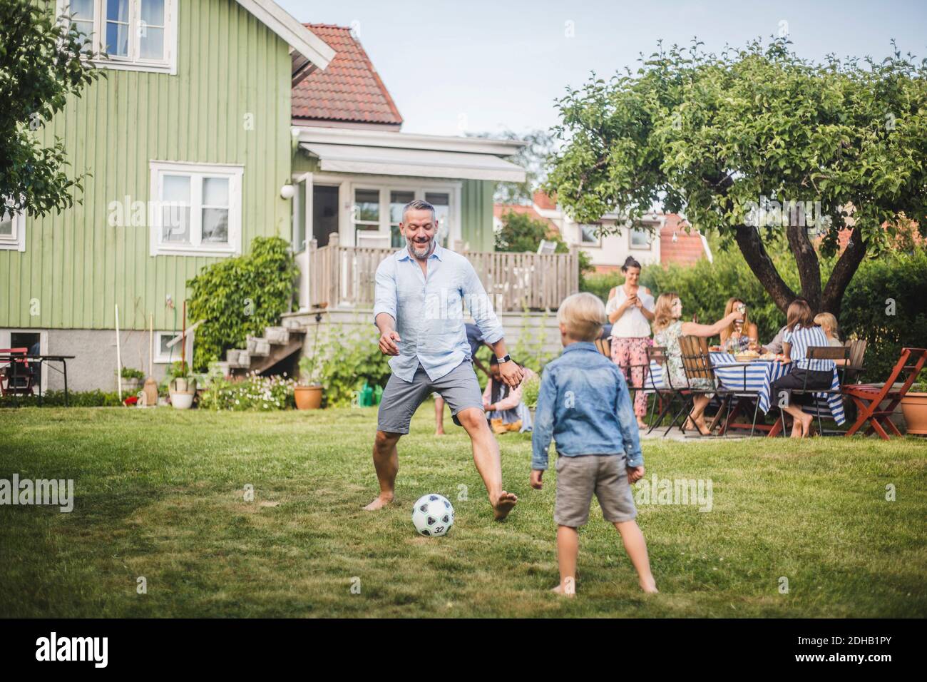 Vater spielt Fußball mit Sohn, während Freunde Spaß haben Tisch im Hinterhof Party Stockfoto