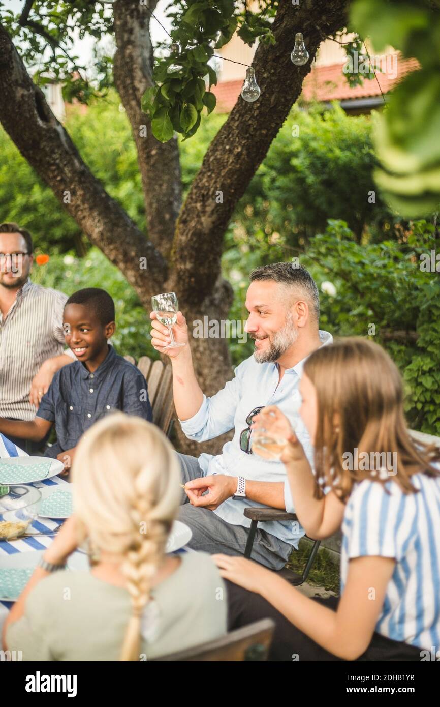 Reifer Mann heben Weinglas während sitzen mit Freund und Kinder im Hinterhof Party Stockfoto
