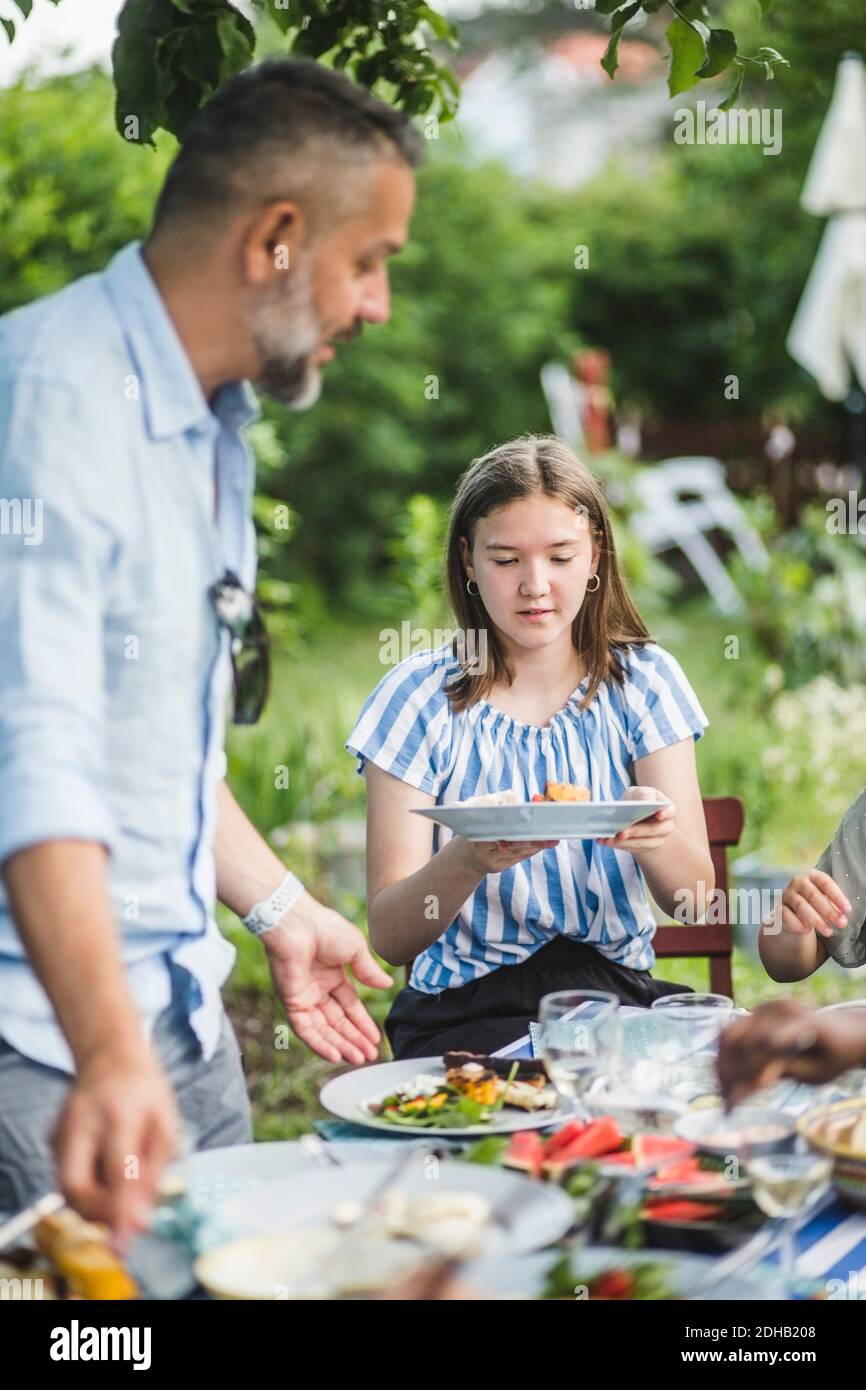 Mädchen hält Teller während sitzen am Tisch mit Familie Im Hinterhof Stockfoto