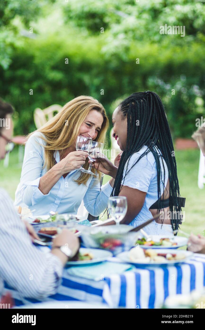 Glückliche Freundinnen toasten Weingläser am Esstisch während des Gartens Party Stockfoto