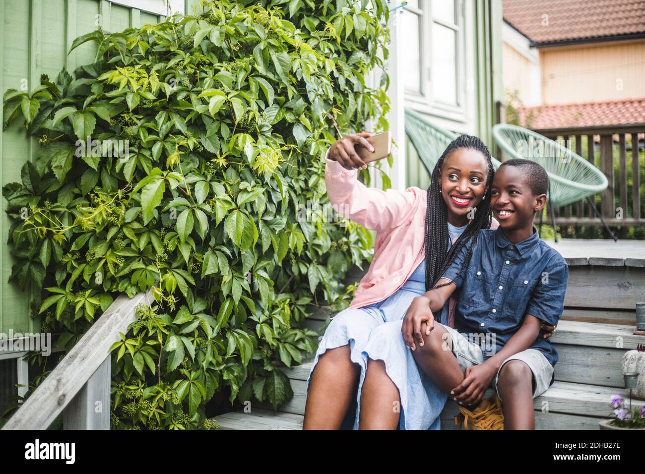 Mutter nimmt Selfie über Smartphone, während sie bei Pflanzen sitzt Auf Stufen Stockfoto