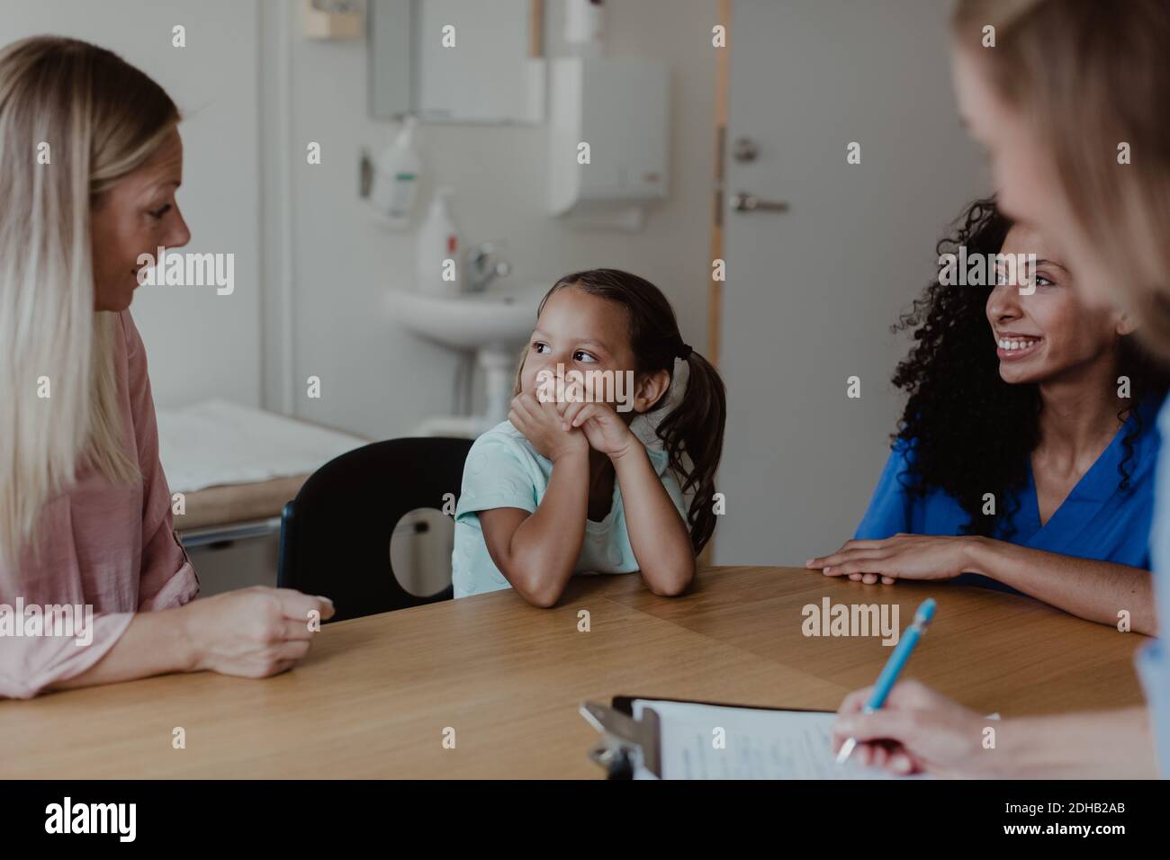 Mutter im Gespräch mit Mädchen, während medizinische Fachkräfte sie betrachten Im Untersuchungsraum Stockfoto