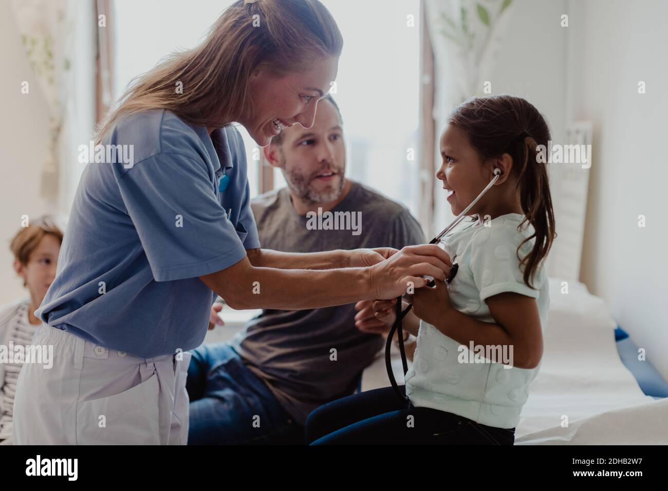 Lächelnder Doktor, der Mädchen beim Hören ihrer eigenen Herzschläge hilft Krankenhaus Stockfoto