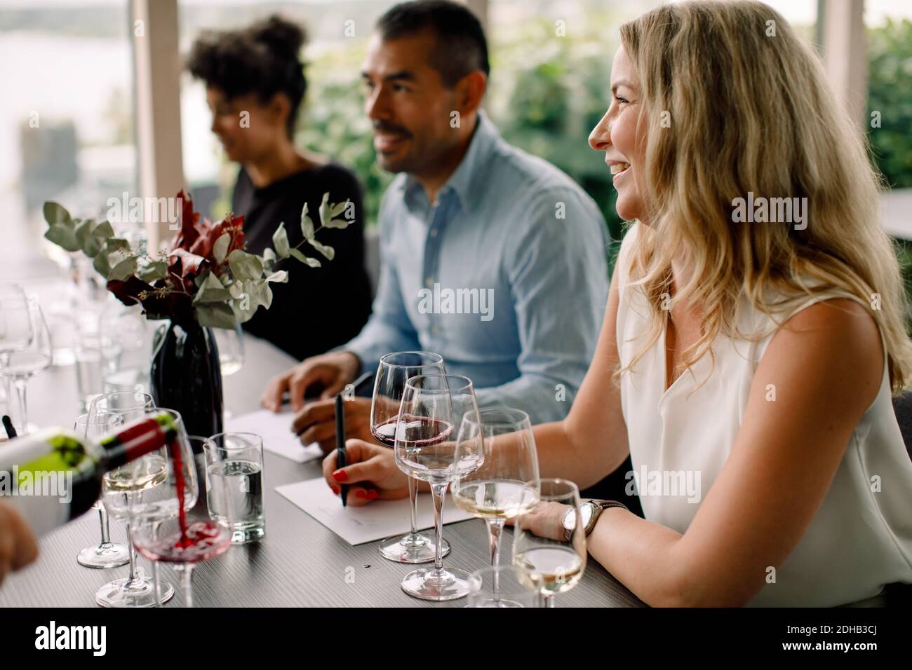 Lächelnde Geschäftsfrau, die wegschaut, während sie mit Kollegen am Tisch sitzt Im Convention Center Stockfoto