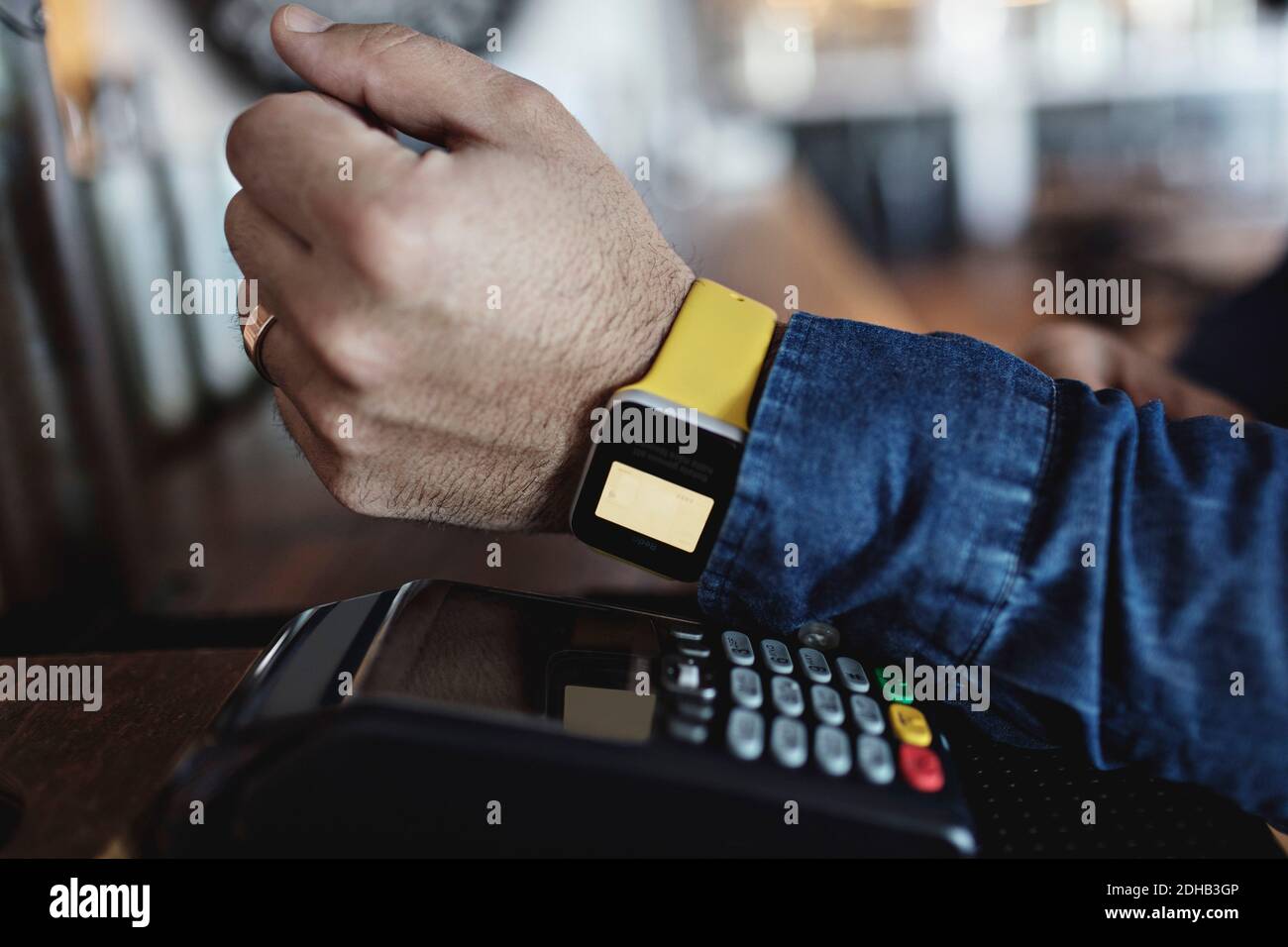 Zugeschnittenes Bild des Kunden, der kontaktlos über Smart Watch bezahlt Am Barschalter Stockfoto