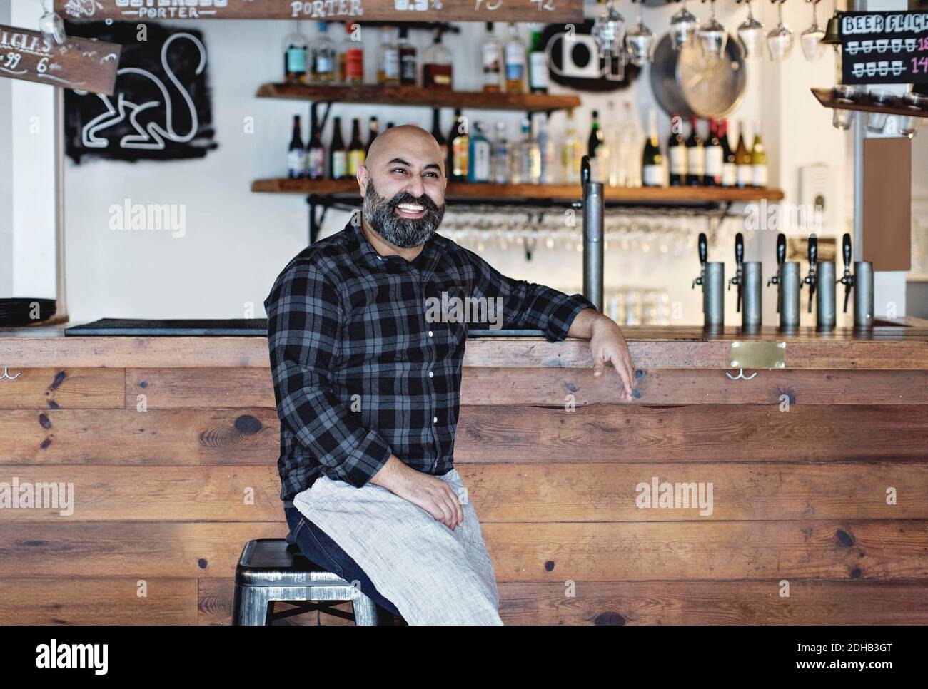 Selbstbewusster, lächelnder Barkeeper, der an der Theke sitzt Stockfoto
