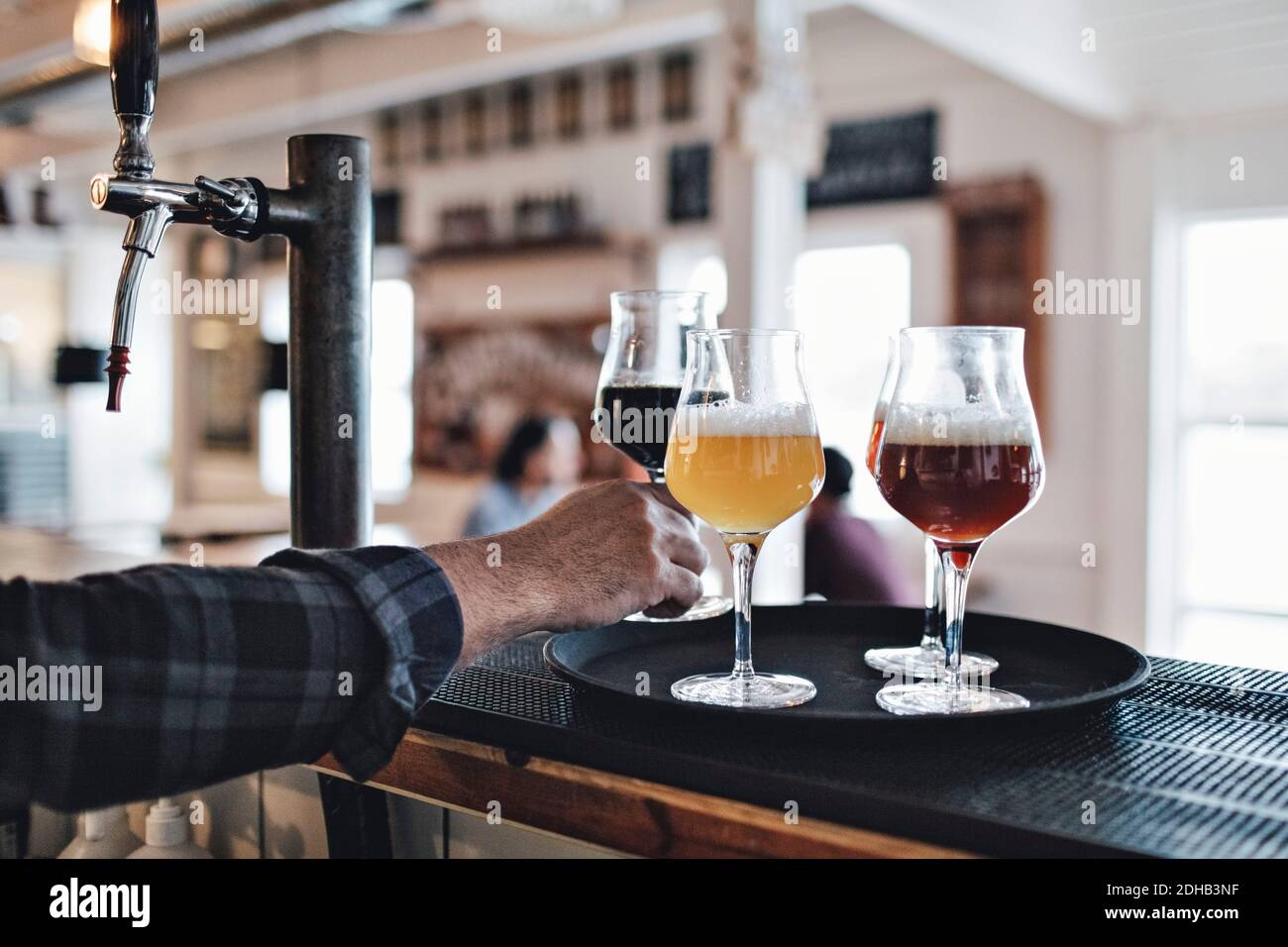 Zugeschnittenes Bild von Barkeeper hält Bierglas auf Tablett bei Zähler Stockfoto
