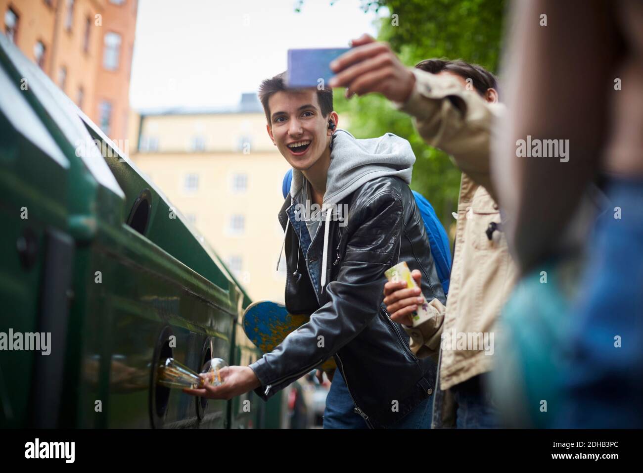 Mann, der Selfie mit einem Teenager-Freund nimmt, der Abfall in den Müll wirft Behälter an der Recyclingstation Stockfoto