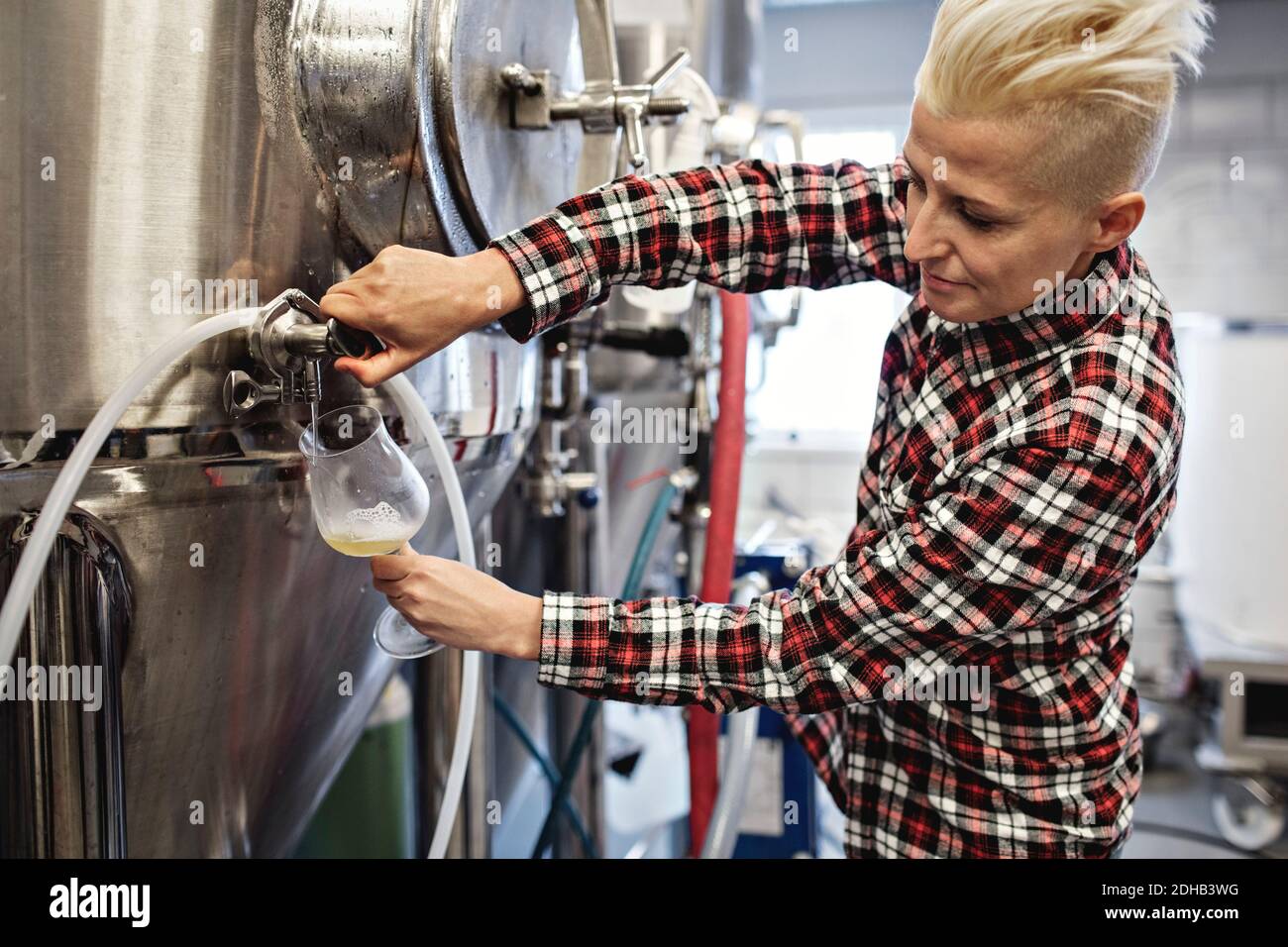 Selbstbewusste Managerin, die Bier aus dem Lagertank im Werk gießt Stockfoto