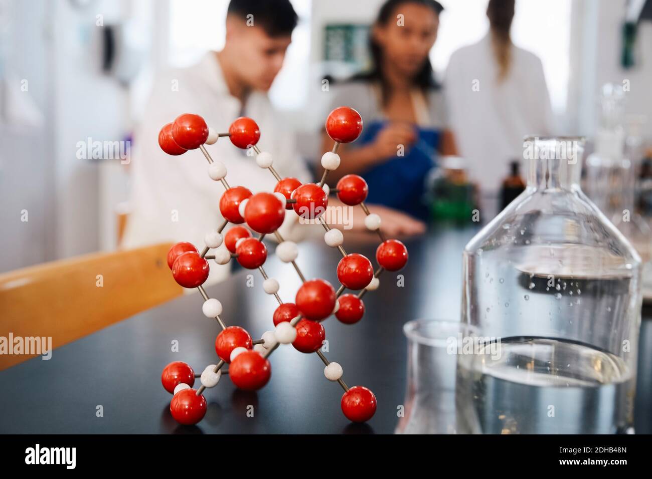 Molekulare Struktur von Glaswaren auf dem Tisch gegen junge Studenten in Chemielabor Stockfoto