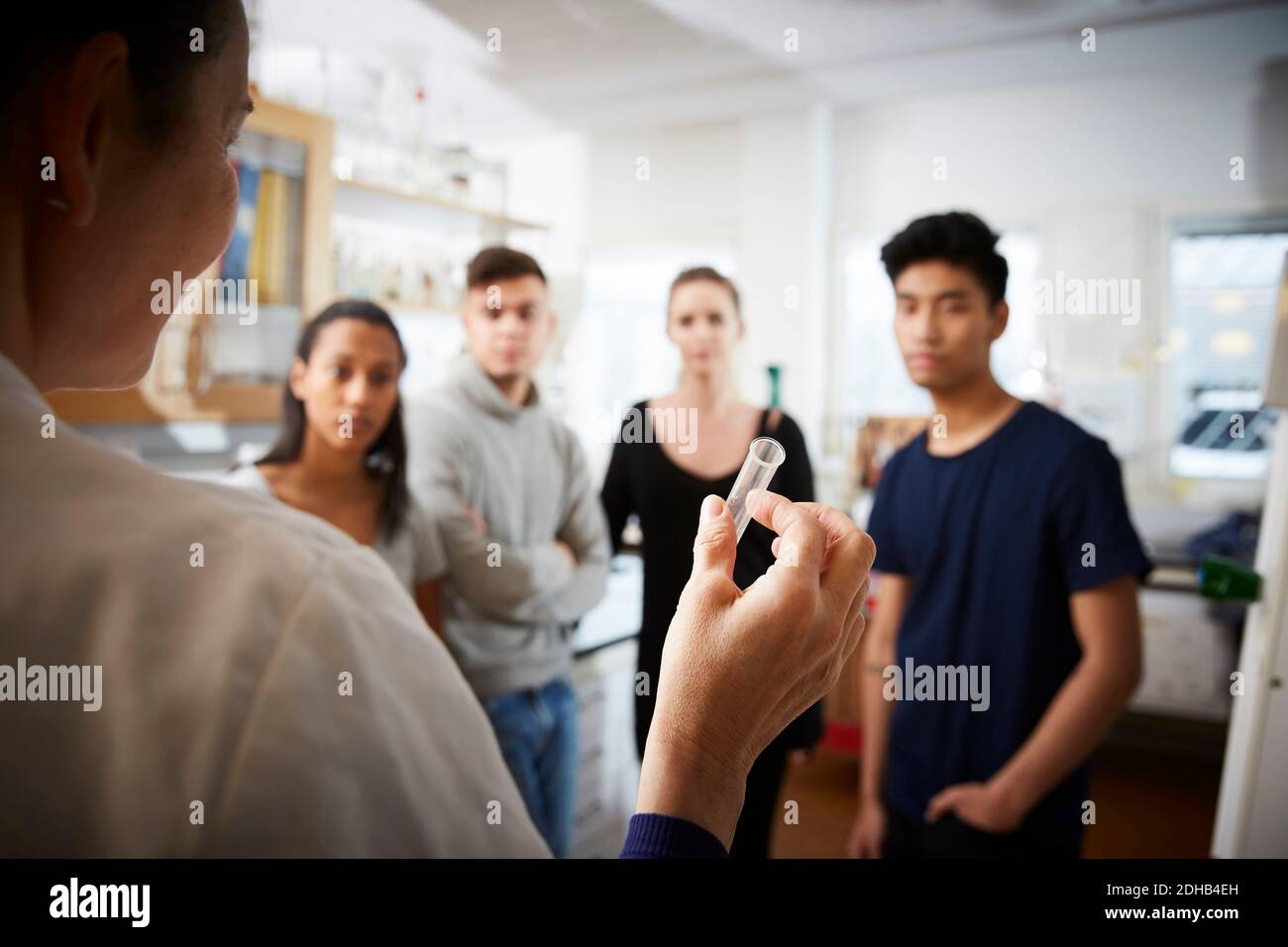 Rückansicht von reifen weiblichen Lehrer hält Reagenzglas erklären An junge multiethnische Studenten im Labor Stockfoto
