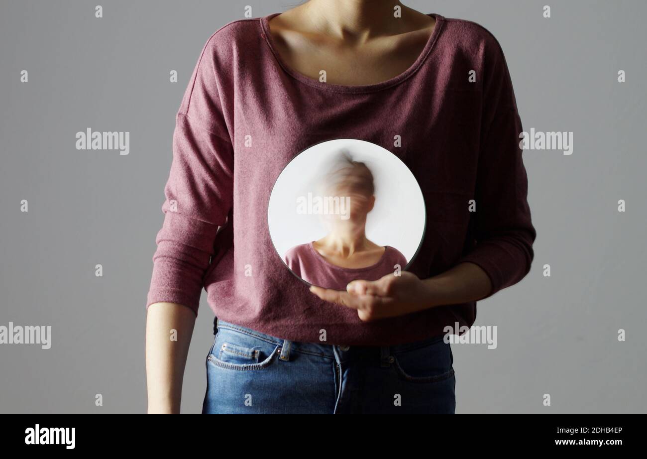 Wer bin ich? Junge Frau, die einen runden Spiegel vor ihrem Körper hält. Der Spiegel zeigt ihr verschwommenes Gesicht. Stockfoto