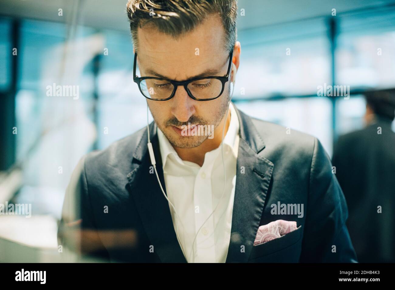 Reifer Geschäftsmann mit Brillen, die Kopfhörer tragen, während er nach unten schaut Büro Stockfoto