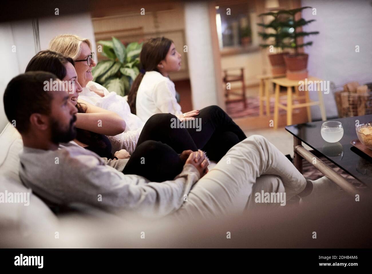 Familie, die Fernsehen schaut, während sie auf dem Sofa im Wohnzimmer sitzt Zu Hause Stockfoto