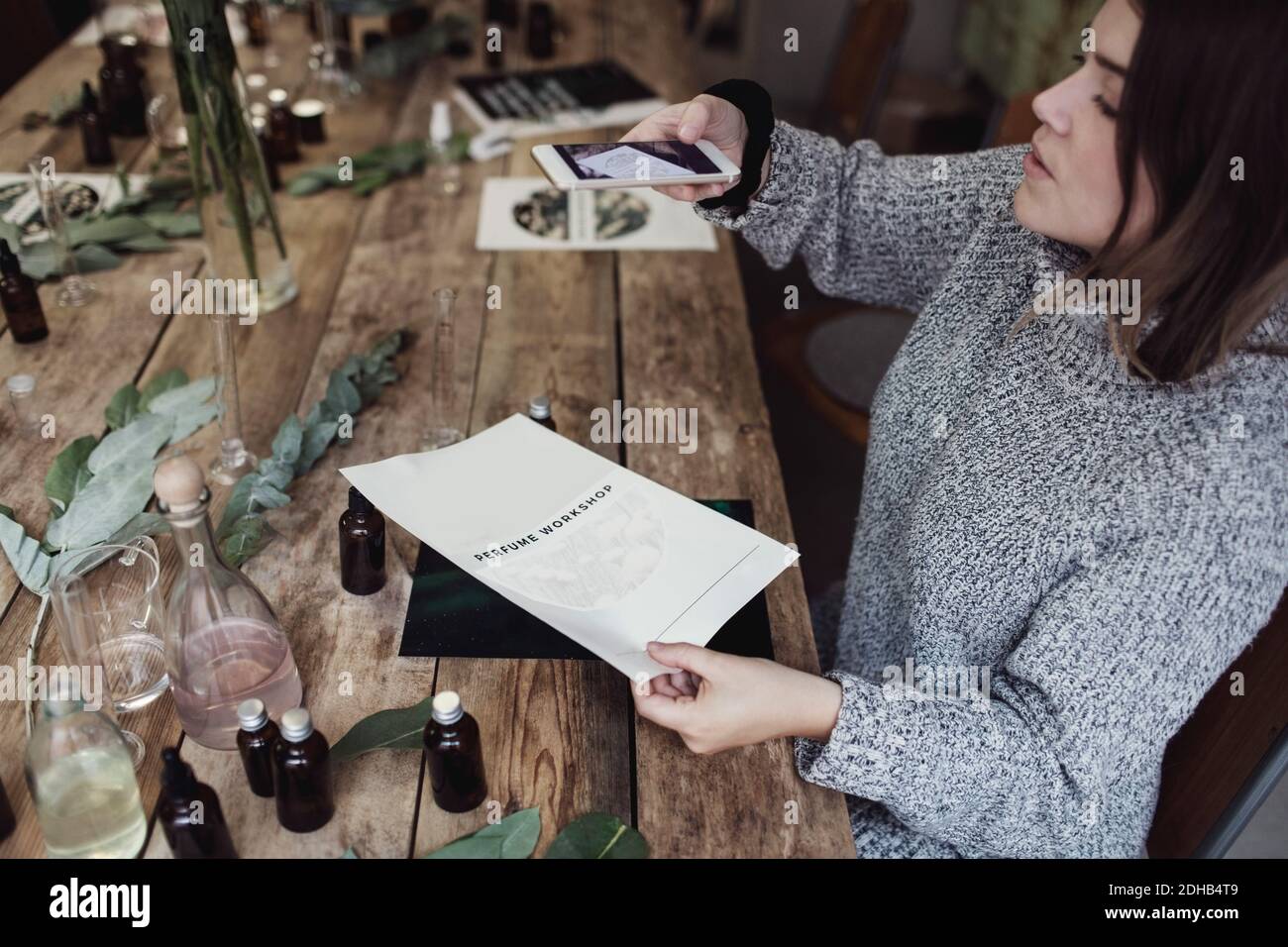Hochwinkelansicht der mittleren erwachsenen weiblichen Besitzerin, die Broschüre fotografiert Beim Sitzen am Tisch in der Werkstatt Stockfoto