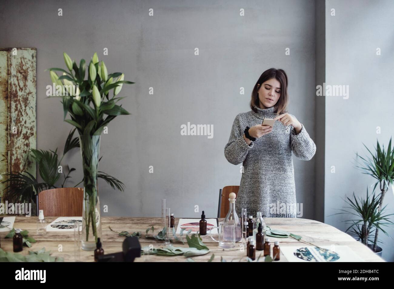 Mittlere Erwachsene weibliche Besitzerin fotografiert verschiedene Flaschen auf dem Tisch Parfüm-Werkstatt Stockfoto