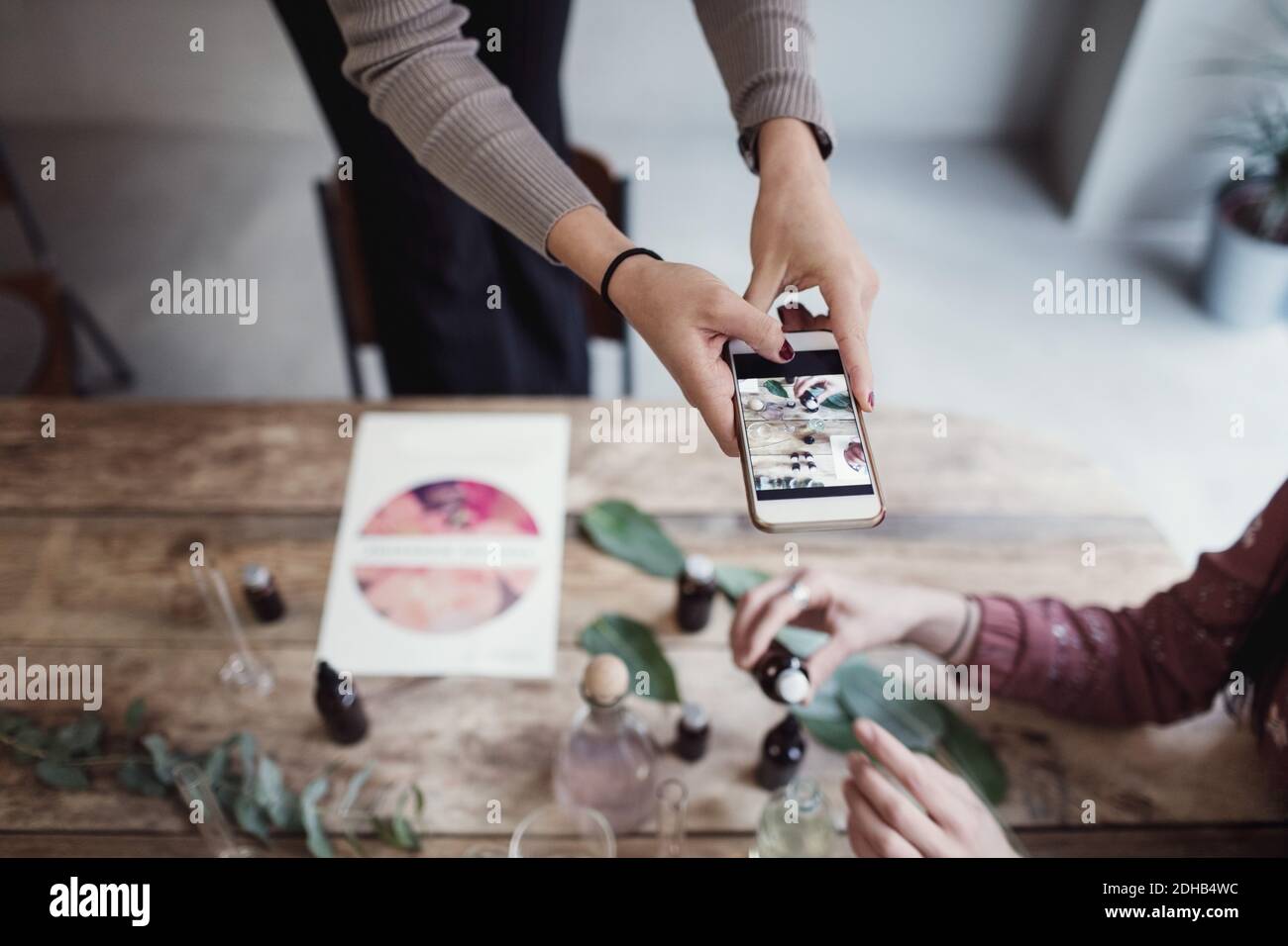 Mittelteil der jungen Frau, die Kollegen hält, die Parfüm am Tisch vorbereiten In der Werkstatt Stockfoto