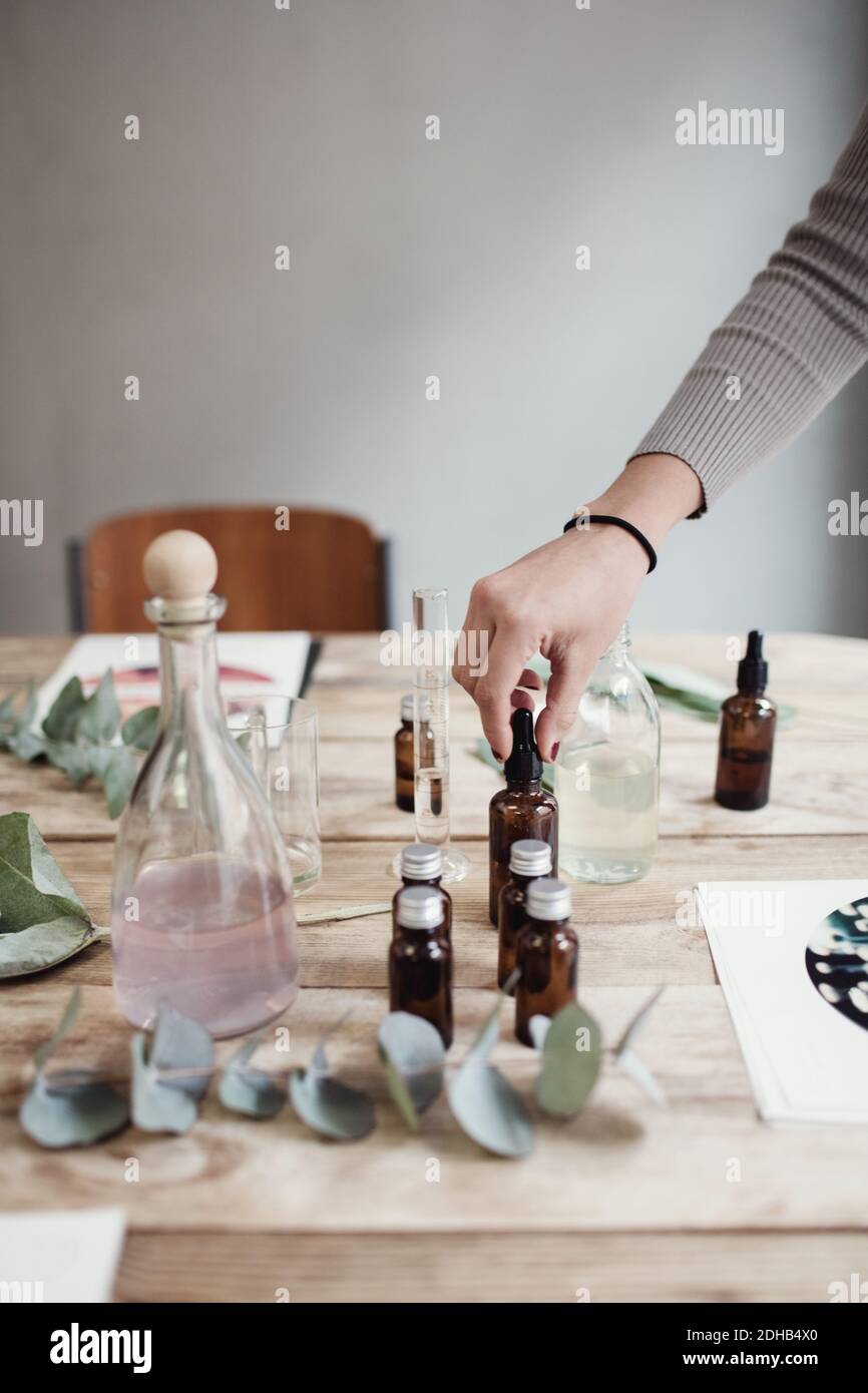 Verkürzte Hand der jungen Frau hält Parfüm Flasche auf dem Tisch In der Werkstatt Stockfoto