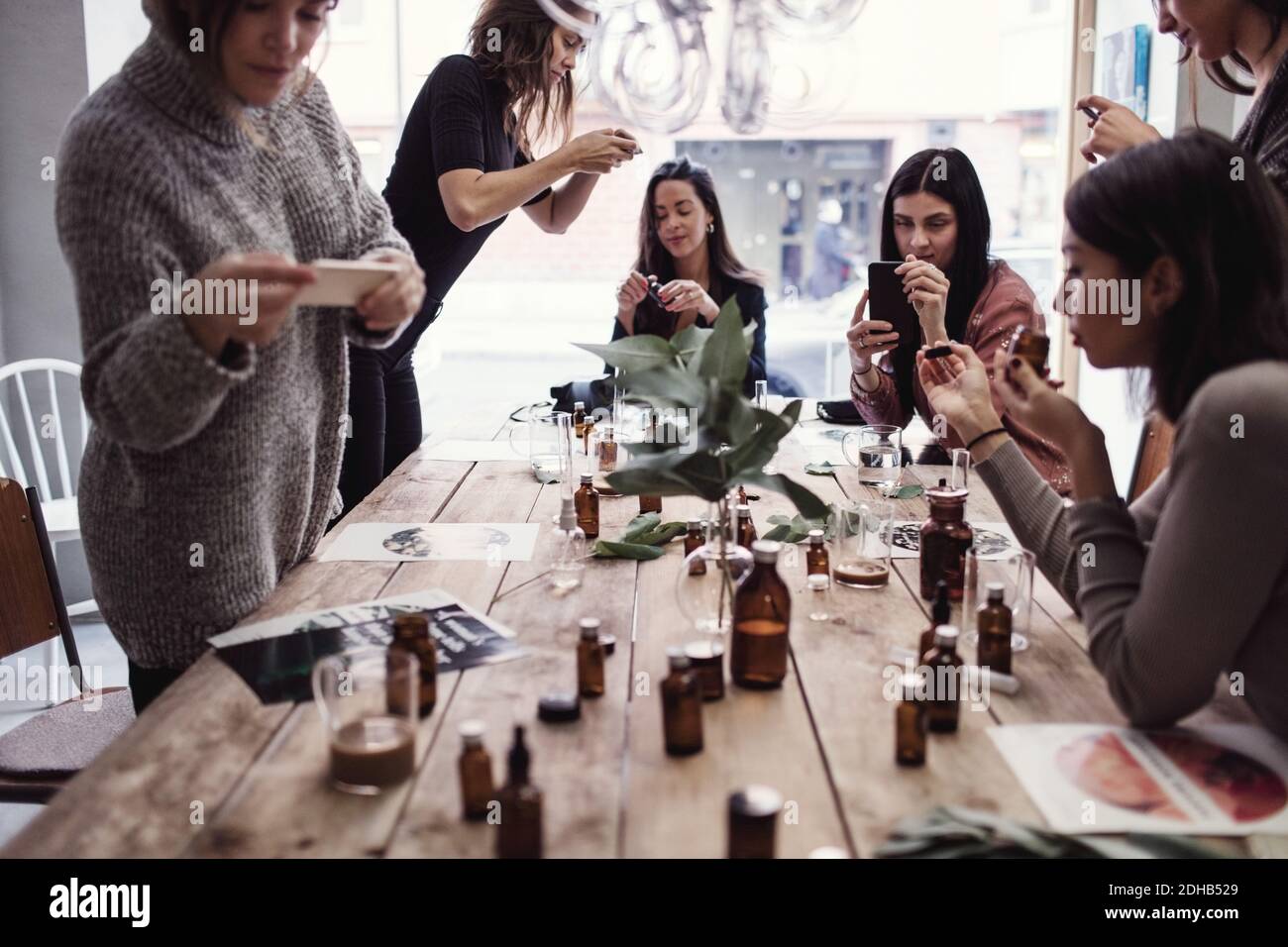 Multiethnische weibliche Mitarbeiter fotografieren Parfums auf dem Tisch in der Werkstatt Stockfoto