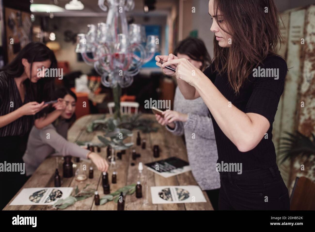 Frau mit mittlerem Erwachsenen, die im Stehen von einem Smartphone aus fotografiert Weibliche Kollegen in der Parfüm-Werkstatt Stockfoto
