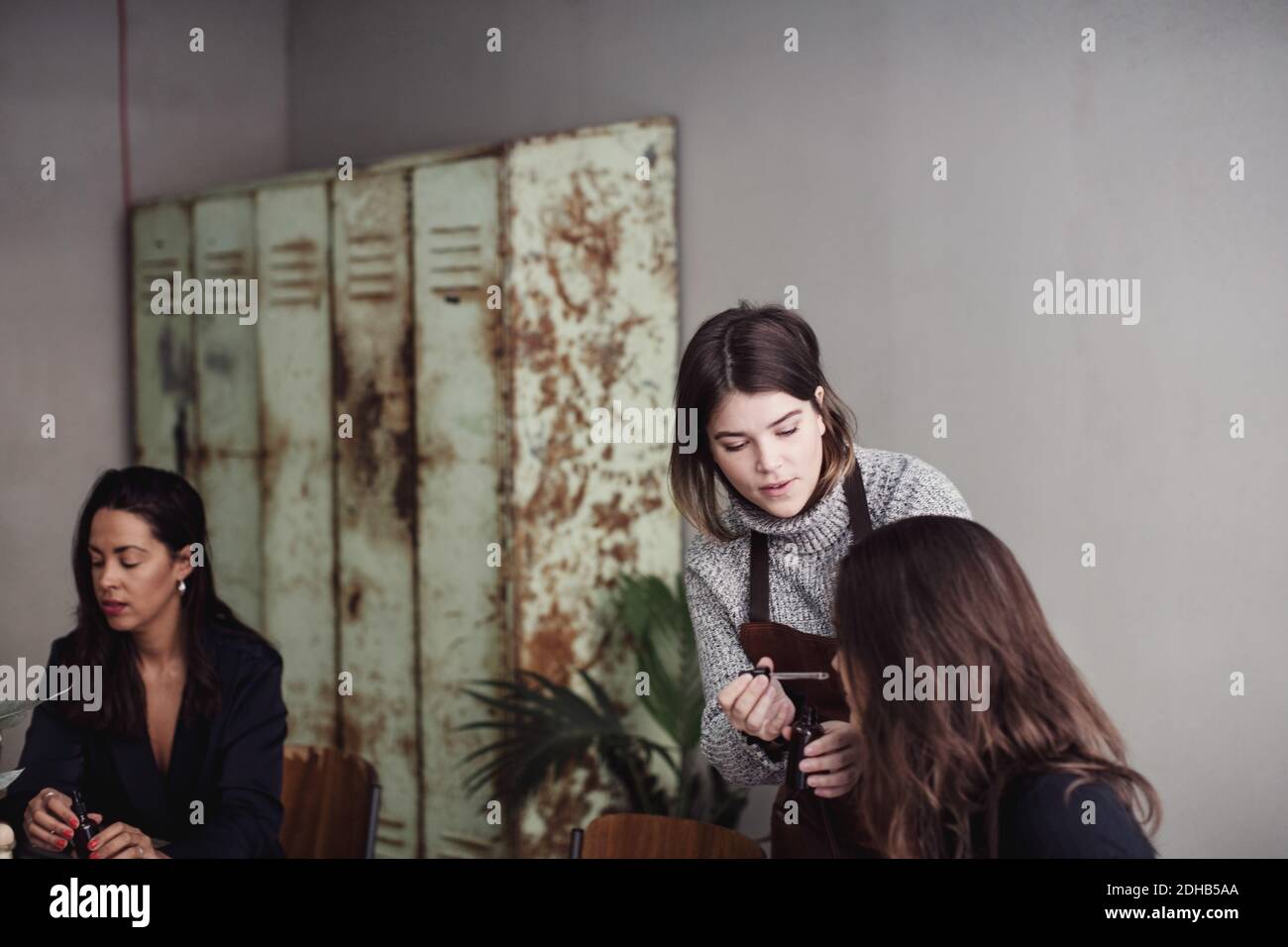 Mittlere Erwachsene weibliche Besitzerin mit Kollegen riechendem Parfüm aus der Pipette In der Werkstatt Stockfoto