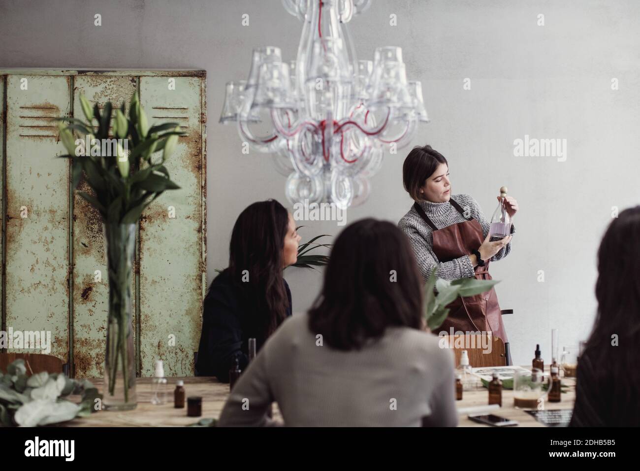 Mittlere Erwachsene weibliche Besitzerin zeigt Parfüm Flasche Kollegen sitzen In der Werkstatt Stockfoto