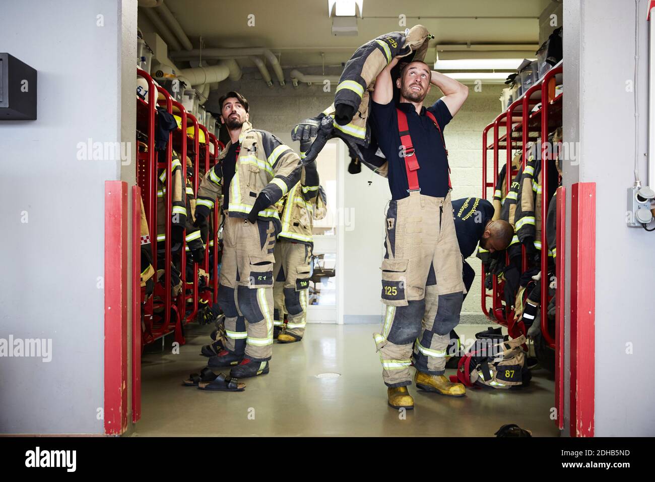 Feuerwehrleute tragen Arbeitsschutzkleidung im Umkleideraum, während sie nach oben schauen An der Feuerwehr Stockfoto