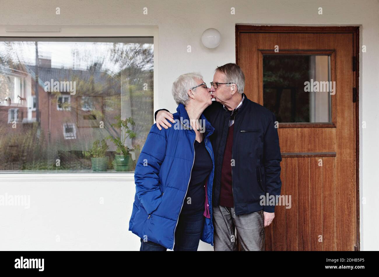 Rentnerehepaar küsst sich, während es gegen das Haus steht Stockfoto