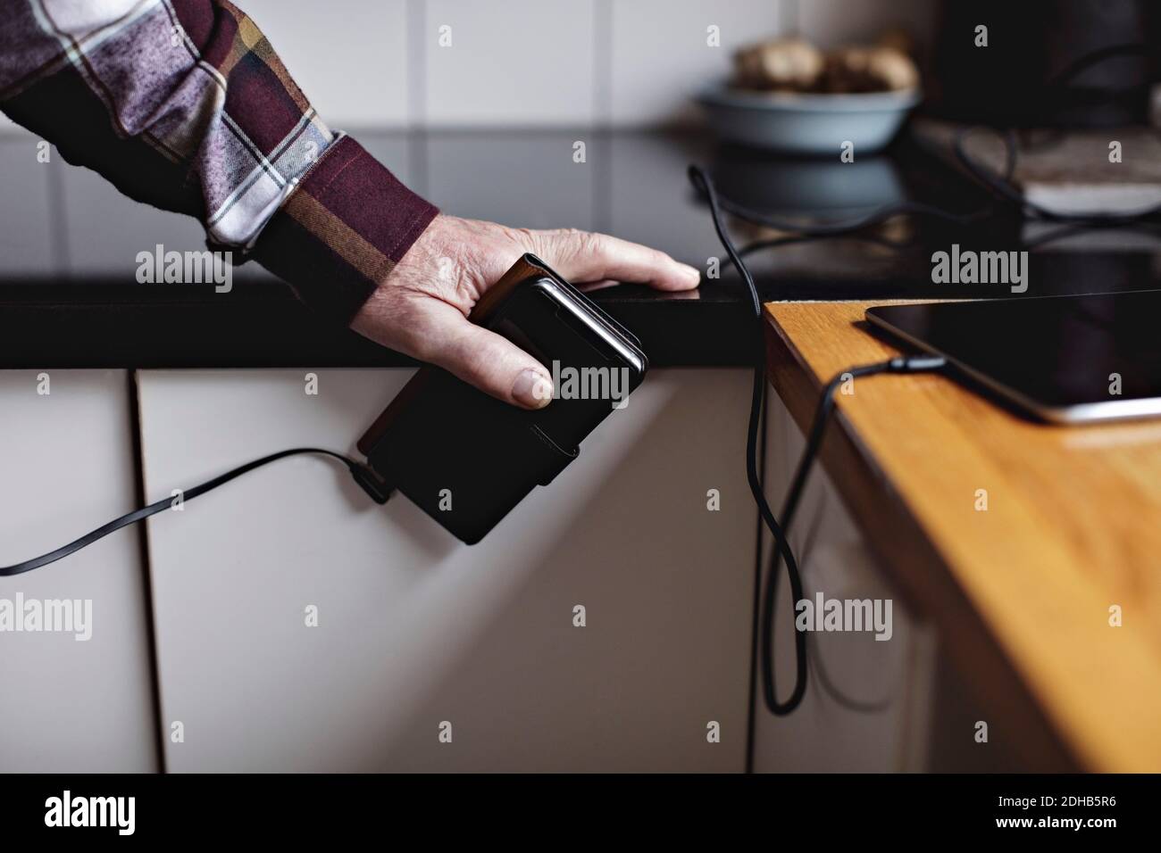 Kurze Hände eines älteren Mannes, der in der Küche ein Smartphone hält Zähler Stockfoto