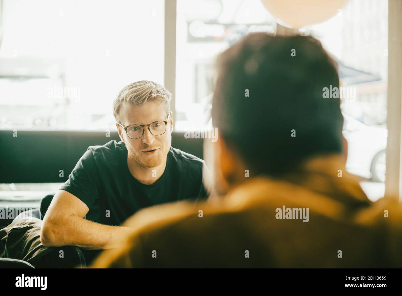 Ein Mann mittleren Erwachsenen, der mit einem Freund spricht, während er im Restaurant sitzt Stockfoto Ein Mann mittleren Erwachsenen, der mit einem Freund spricht, während er im Restaurant sitzt Stockfoto