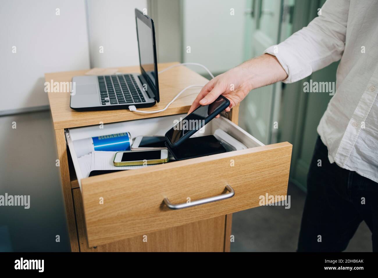Mittelteil des Kursteilnehmers, der Smartphone während der Prüfung in der Schublade hält Stockfoto