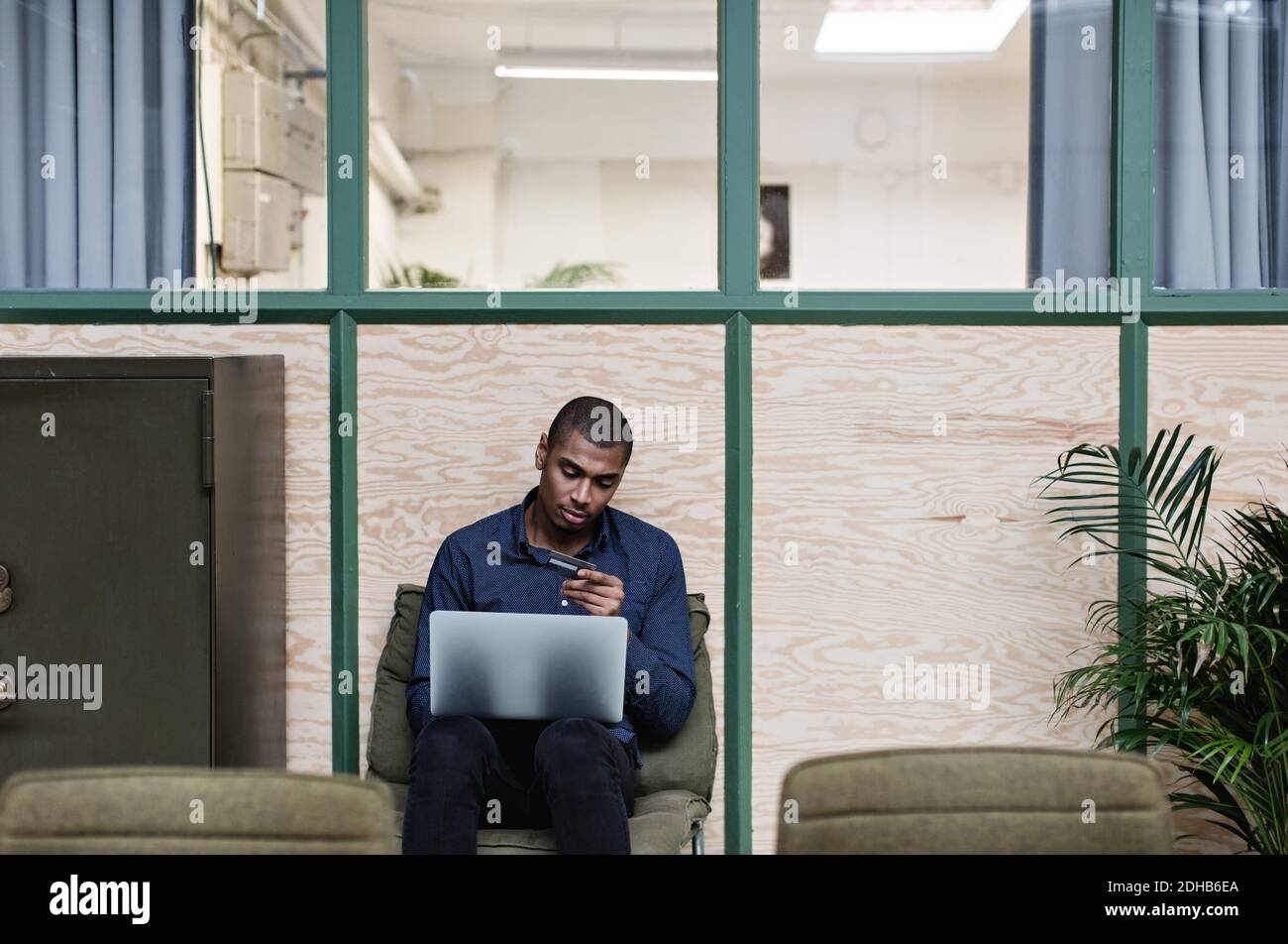 Geschäftsmann beim Online-Shopping mit Kreditkarte über Laptop, während er sitzt Im Kreativbüro Stockfoto