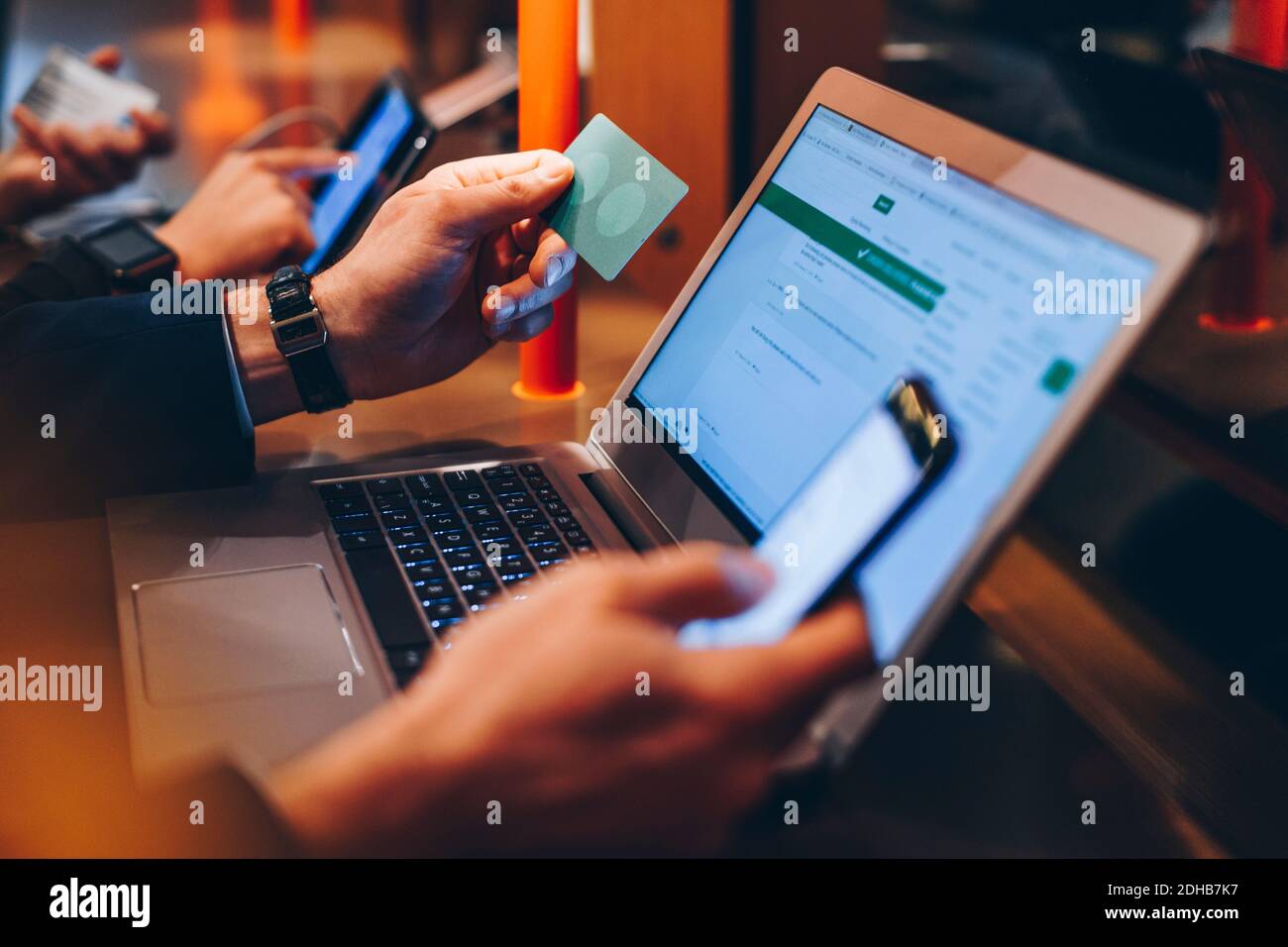 Zugeschnittenes Bild eines Geschäftsmannes, der während der Nutzung eines Mobiltelefons eine Kreditkarte hält Telefon und Laptop am Flughafen Stockfoto