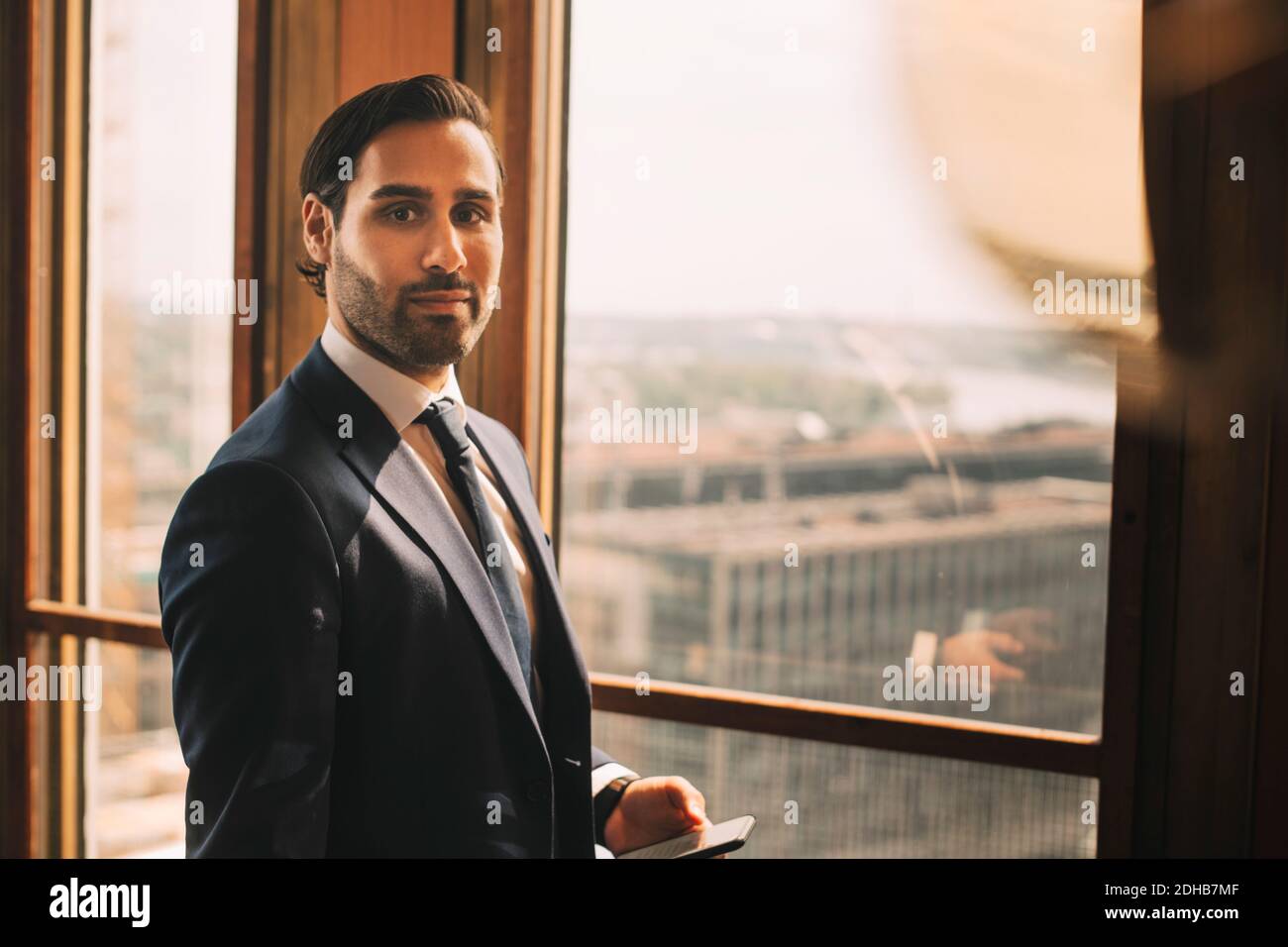 Porträt eines selbstbewussten männlichen Beraters, der bei der Rechtsabteilung am Fenster steht Büro Stockfoto