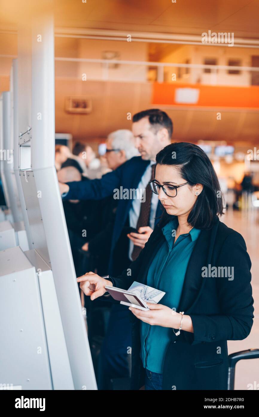 Geschäftsfrau mit Reisepass, während sie den automatischen Check-in-Automaten am Flughafen benutzt Stockfoto