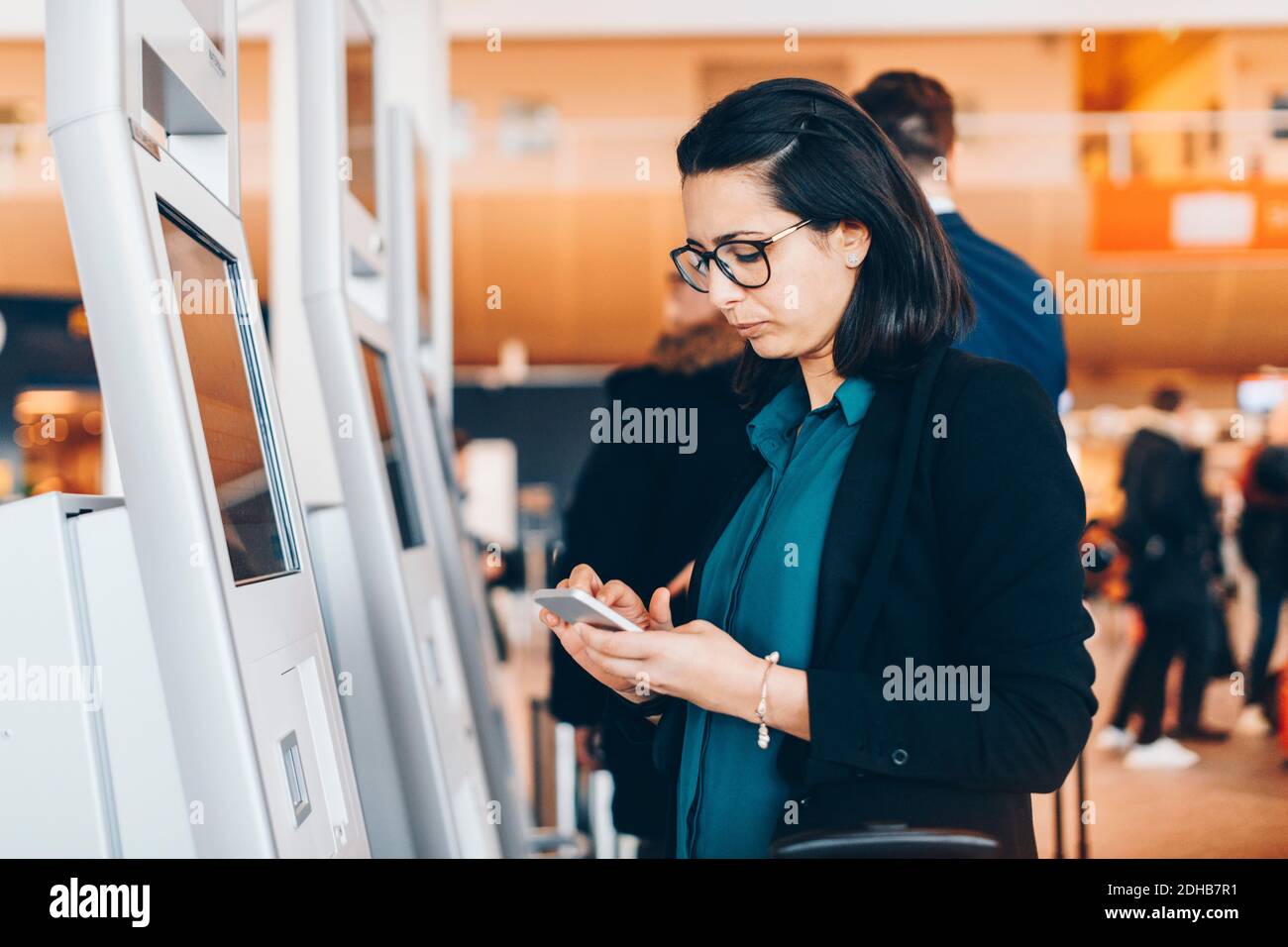 Geschäftsfrau, die am Flughafen ein Mobiltelefon mit einem automatischen Check-in-Automaten nutzt Stockfoto