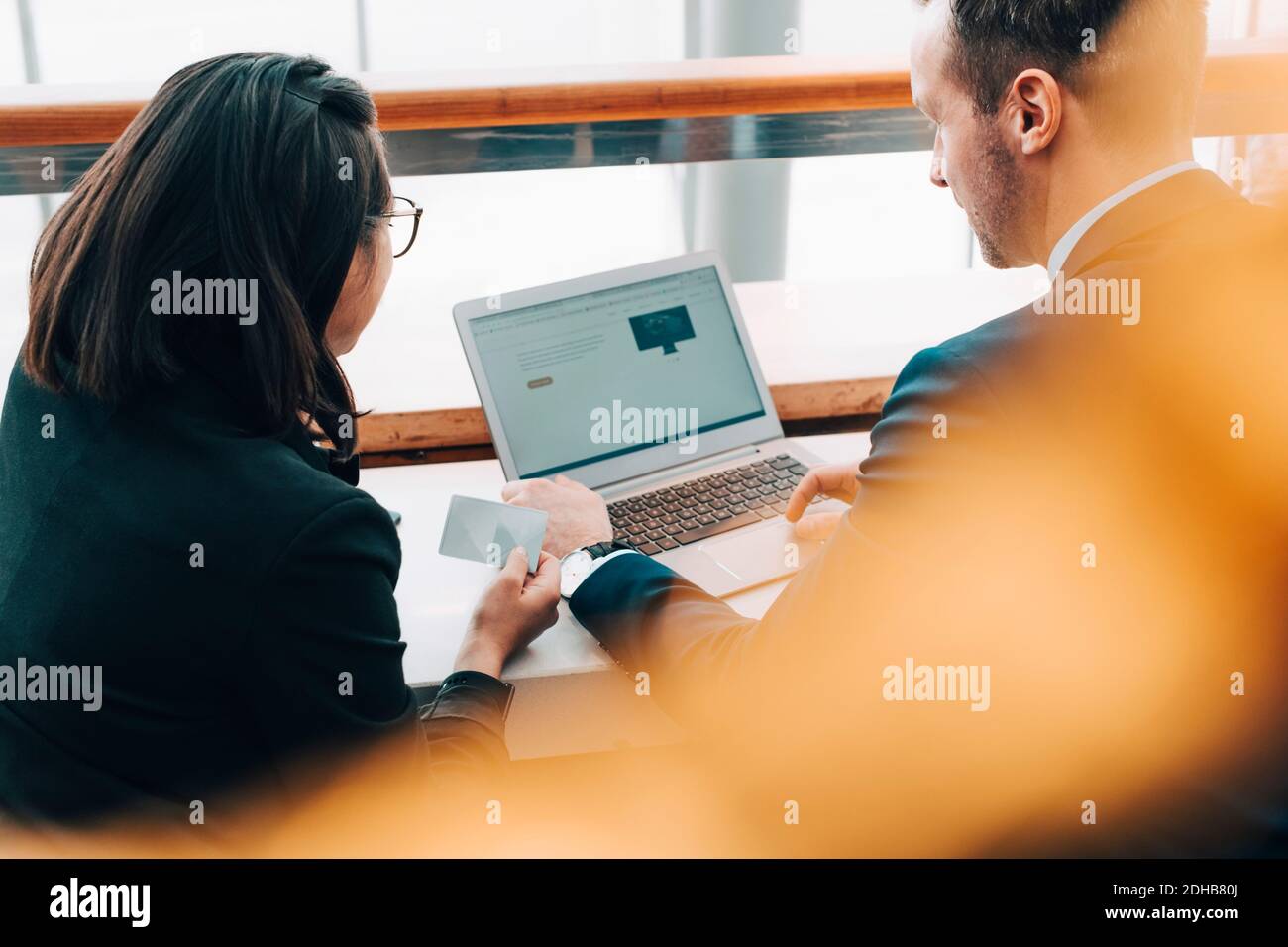 Rückansicht einer Geschäftsfrau mit Kreditkarte während des Geschäftsmannes Laptop im Flughafen Stockfoto