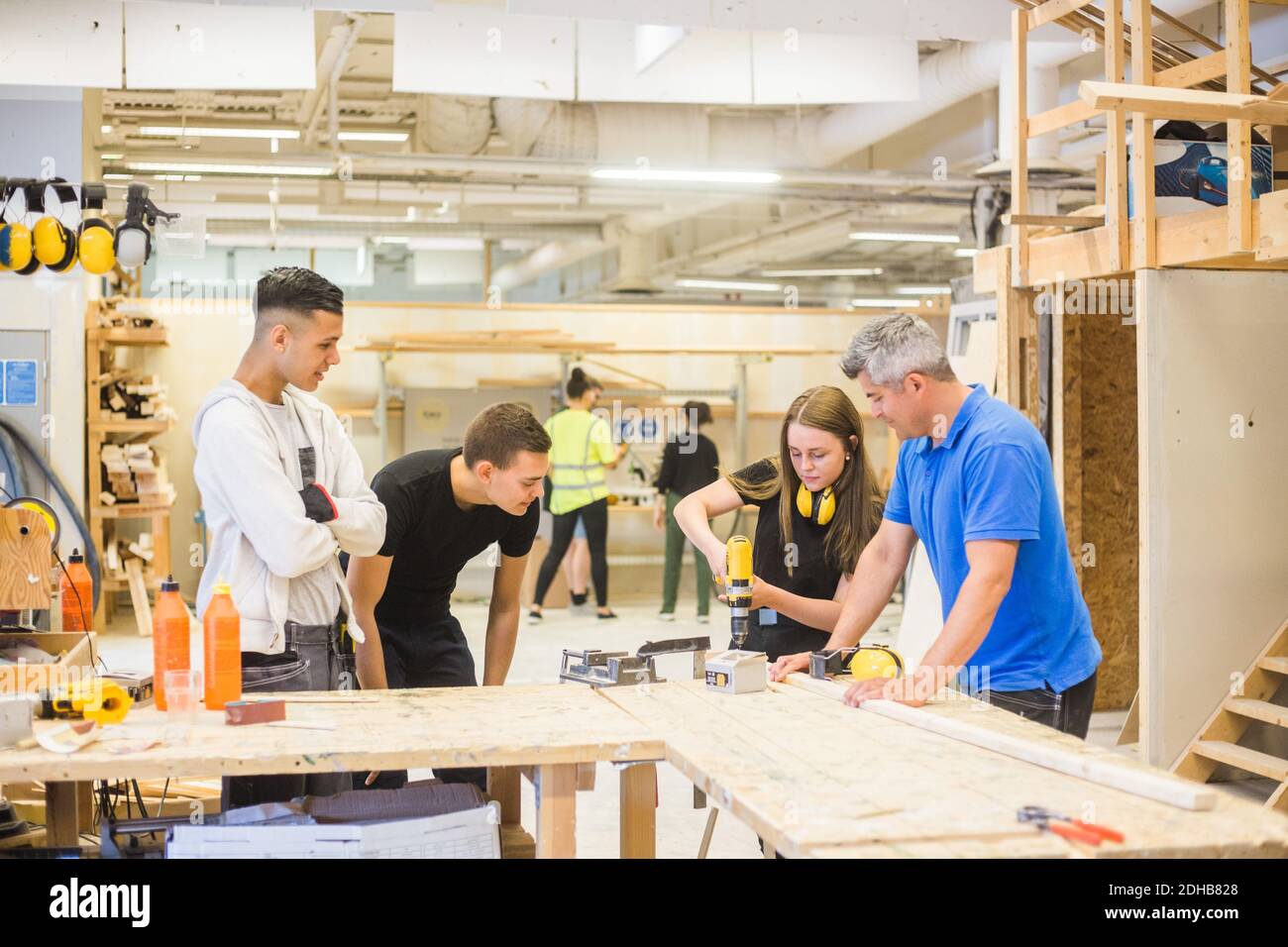 Männlicher Ausbilder und Auszubildende beobachten, während Frau mit Power Drill An der Werkbank während des Trainings Stockfoto