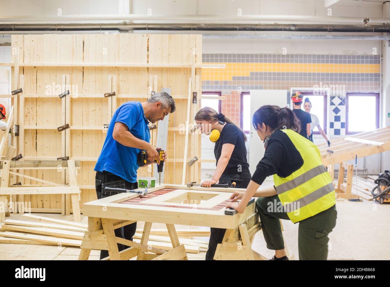 Junge weibliche Auszubildende, die männlichen Ausbilder mit Bohrmaschine betrachten Auf dem Brett an der Werkbank in der Werkstatt Stockfoto
