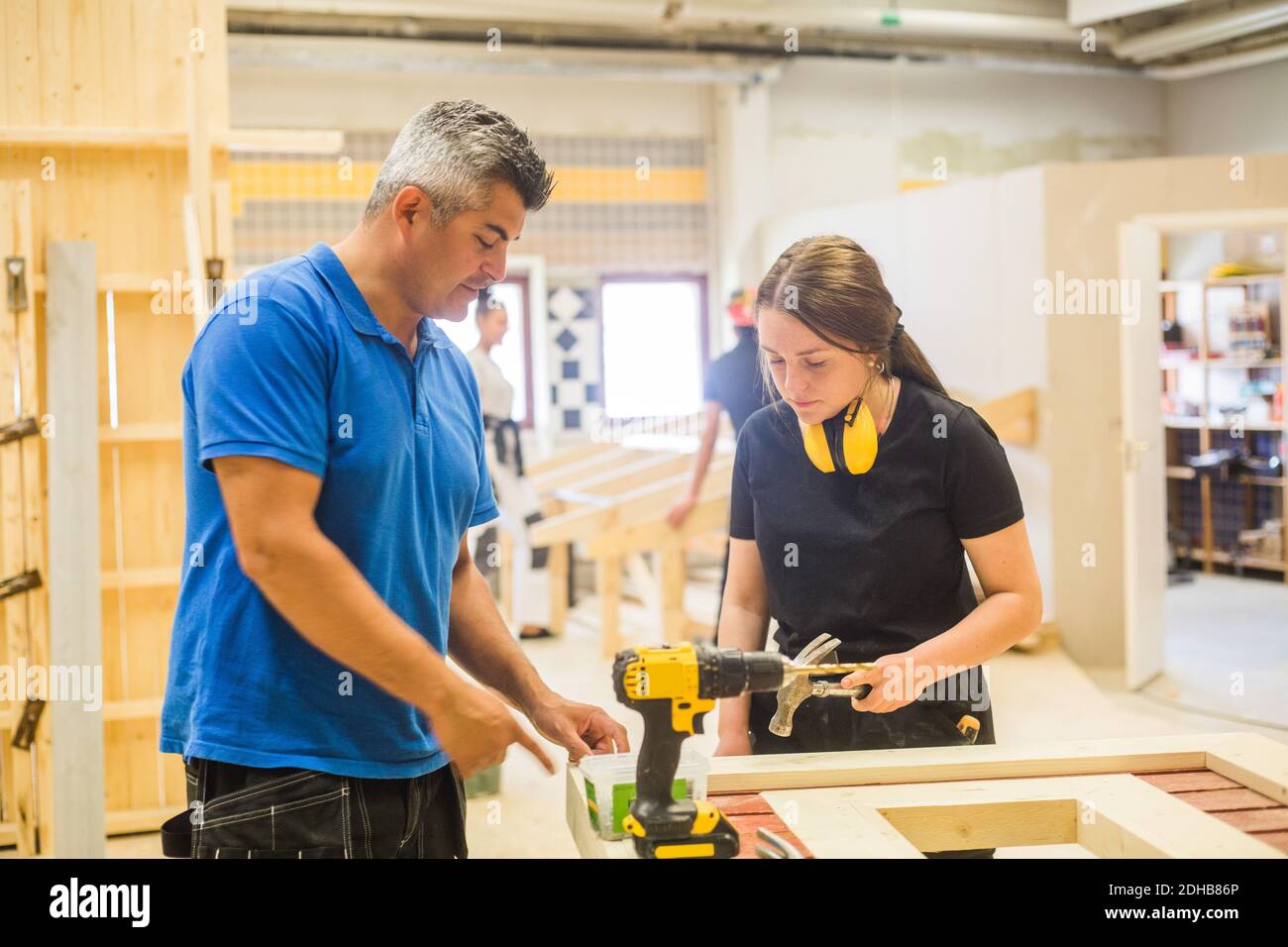 Männlicher Ausbilder unterrichtet weibliche Auszubildende an der Werkbank in beleuchteten Werkstatt Stockfoto