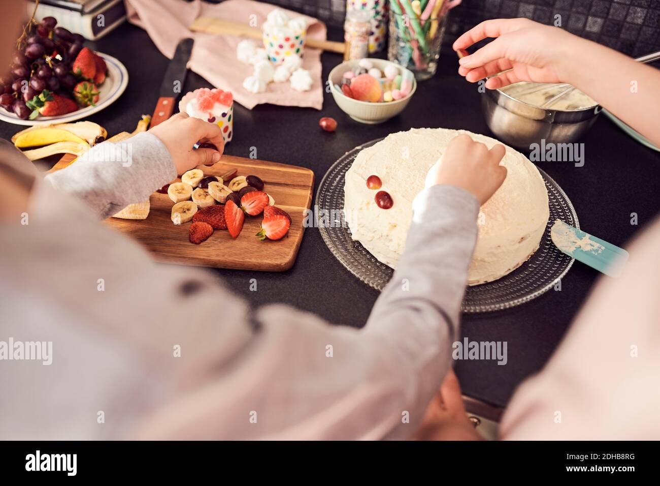 Zugeschnittenes Bild von Geschwistern, die Kuchen an der Küchentheke dekorieren Stockfoto