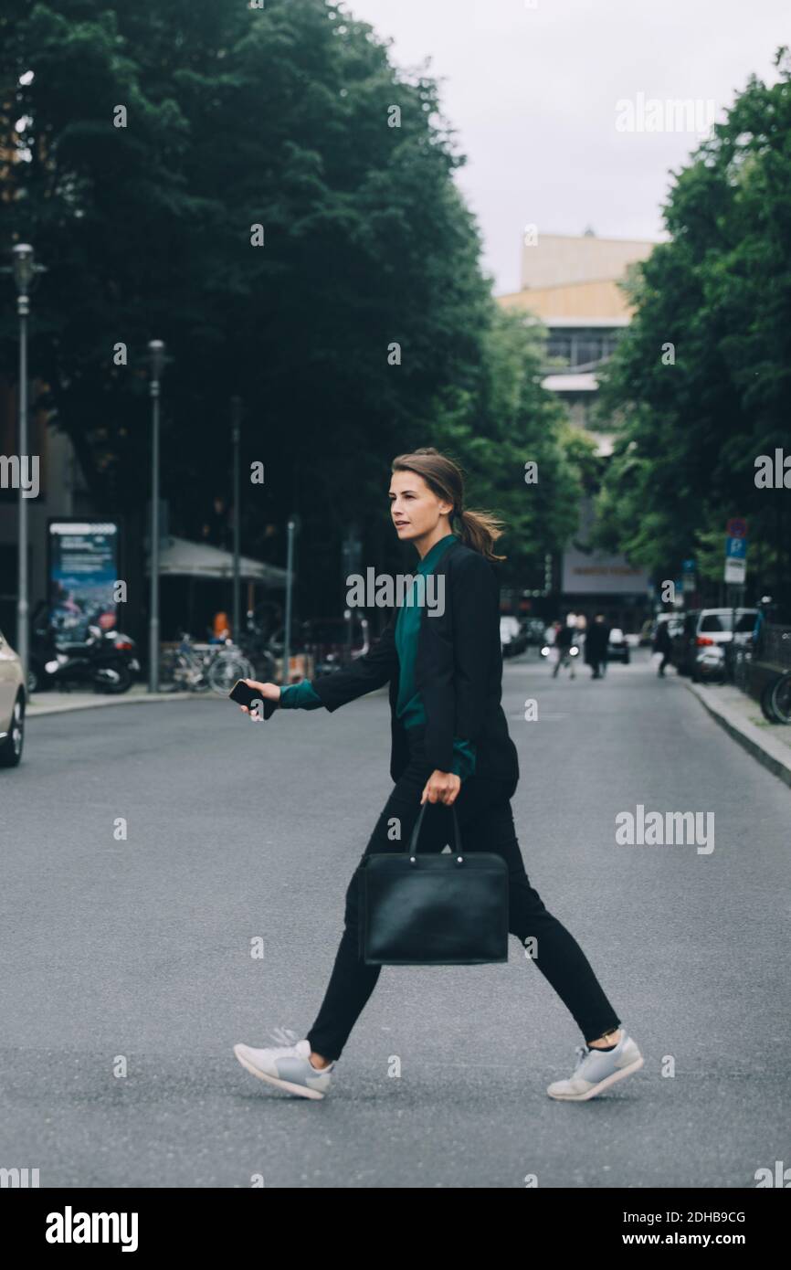 Seitenansicht einer Geschäftsfrau, die die Straße in der Stadt überquert Stockfoto