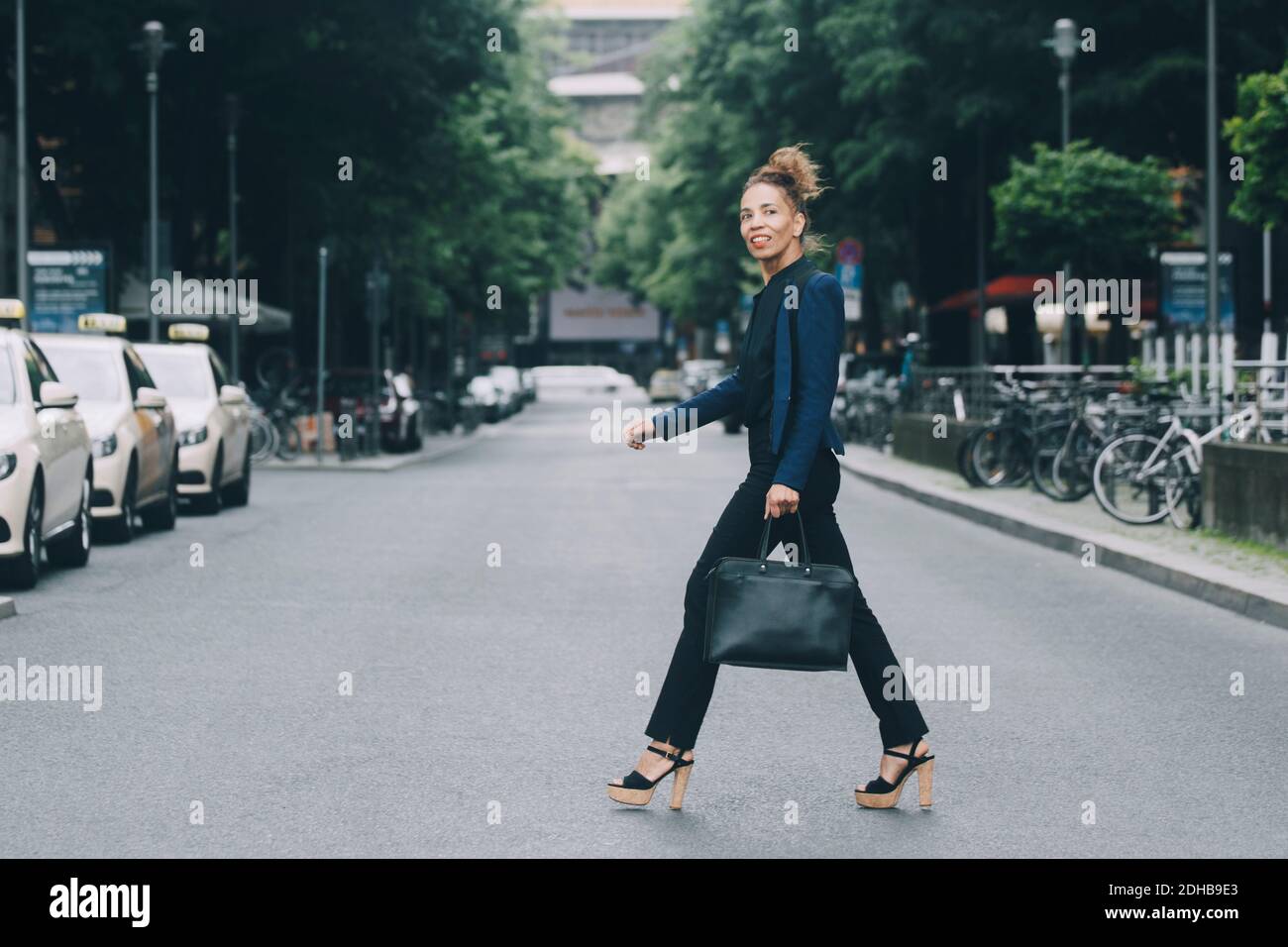 Seitenansicht einer Geschäftsfrau, die die Straße in der Stadt überquert Stockfoto