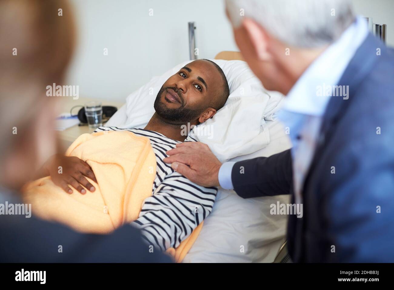 Junger Mann, der die Familie ansieht, während er auf dem Bett liegt Krankenhaus Stockfoto