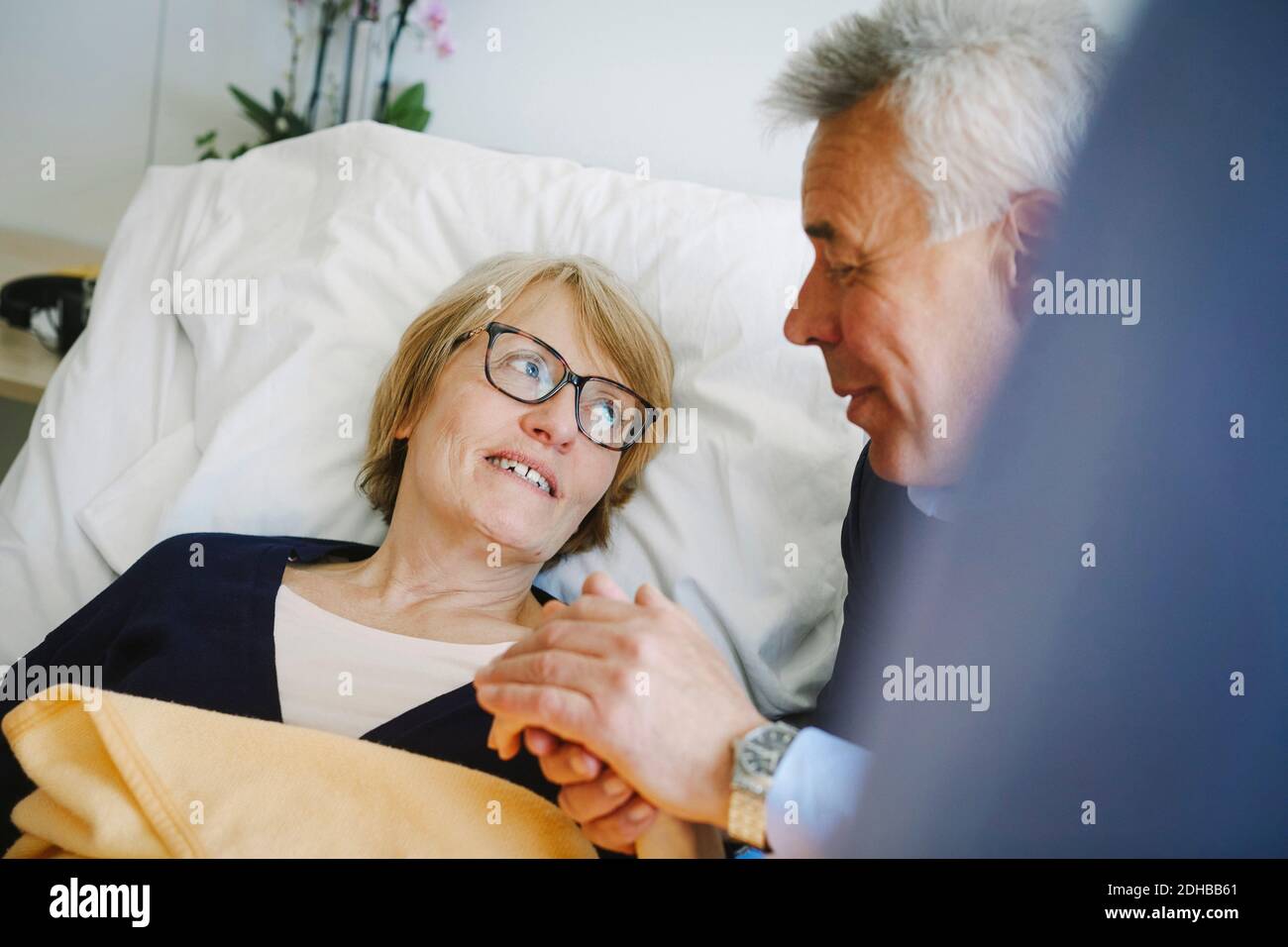Lächelnde Frau, die auf dem Bett liegend zu einem älteren Partner schaut Auf der Krankenstation Stockfoto