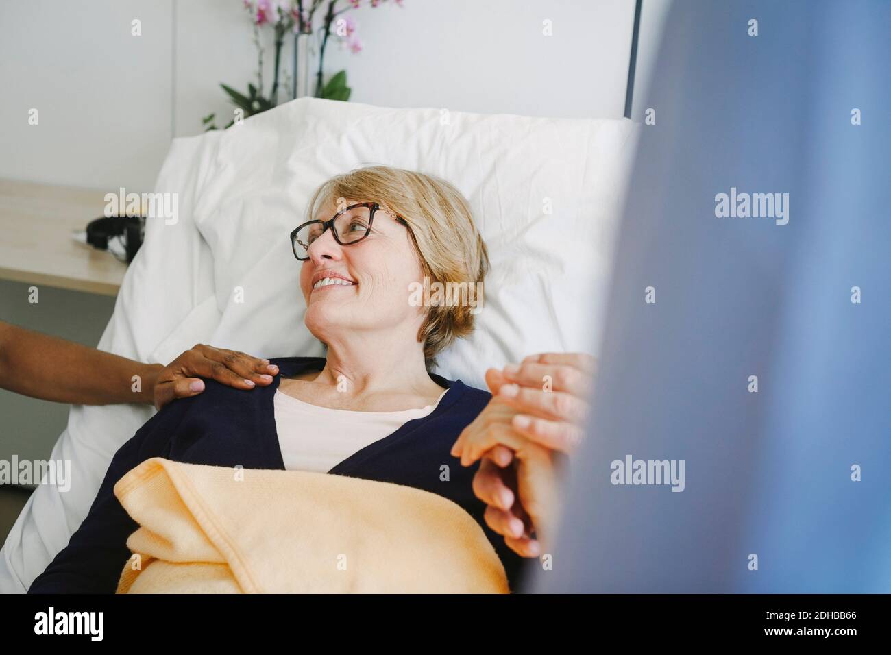 Ältere Frau, die den Arzt ermutigt, während sie die Hände des Partners hält In der Station im Krankenhaus Stockfoto