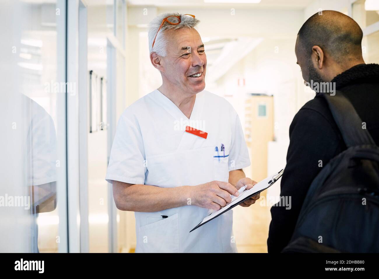 Lächelnder männlicher Arzt erklärt medizinischen Bericht zu männlichen Patienten während Routinebesuch in der Klinik Stockfoto