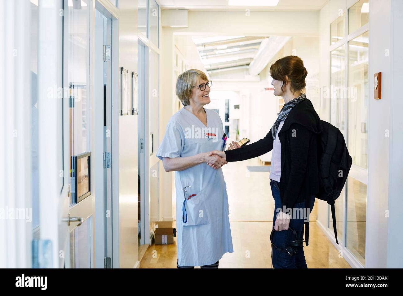 Lächelnde Praktizierende schüttelt sich die Hände mit dem Patienten während des Routinebesuchs Im Krankenhausflur Stockfoto