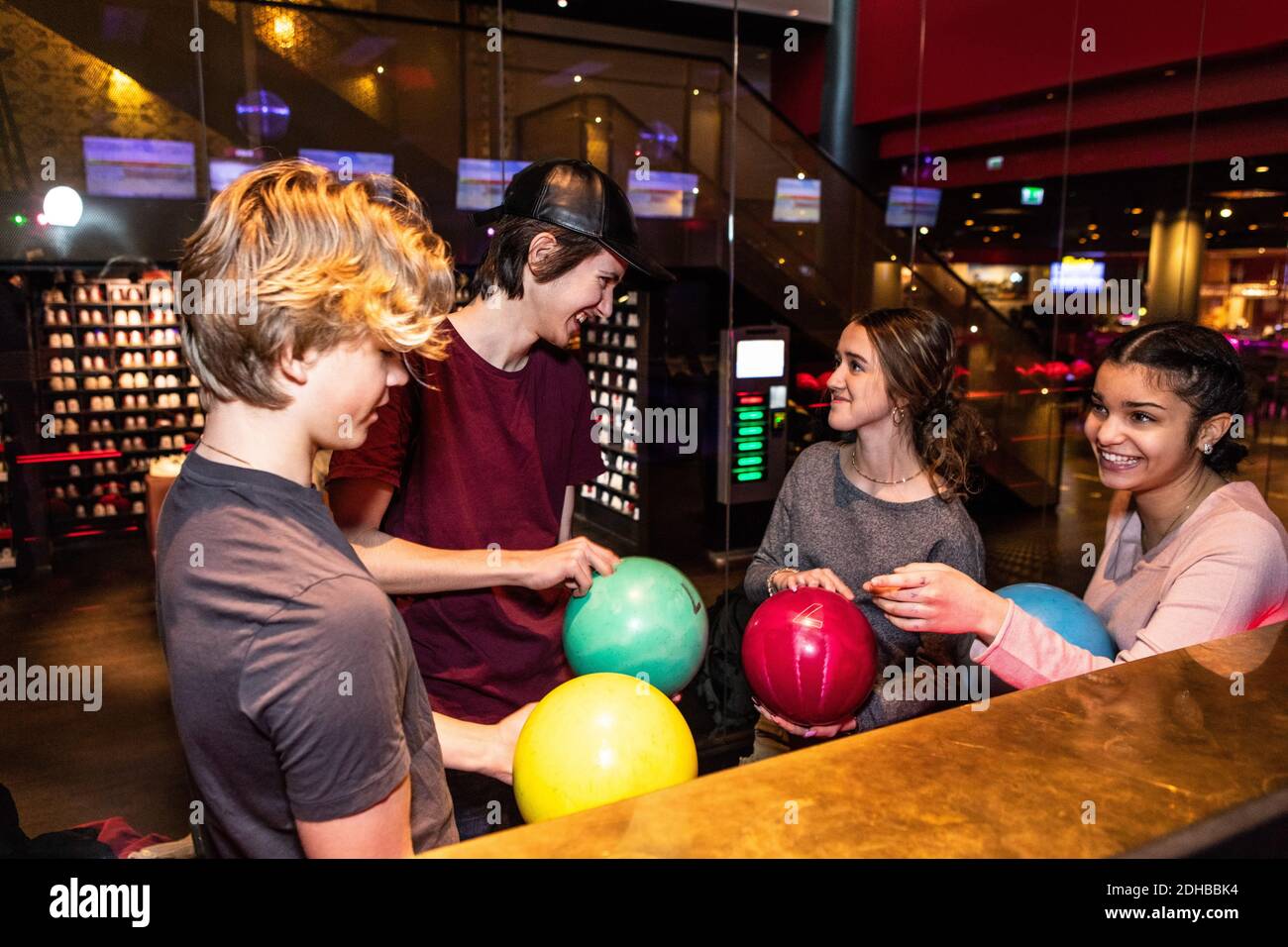 Fröhliche multiethnische Teenager-Freunde stehen mit Bowling-Kugeln Stockfoto