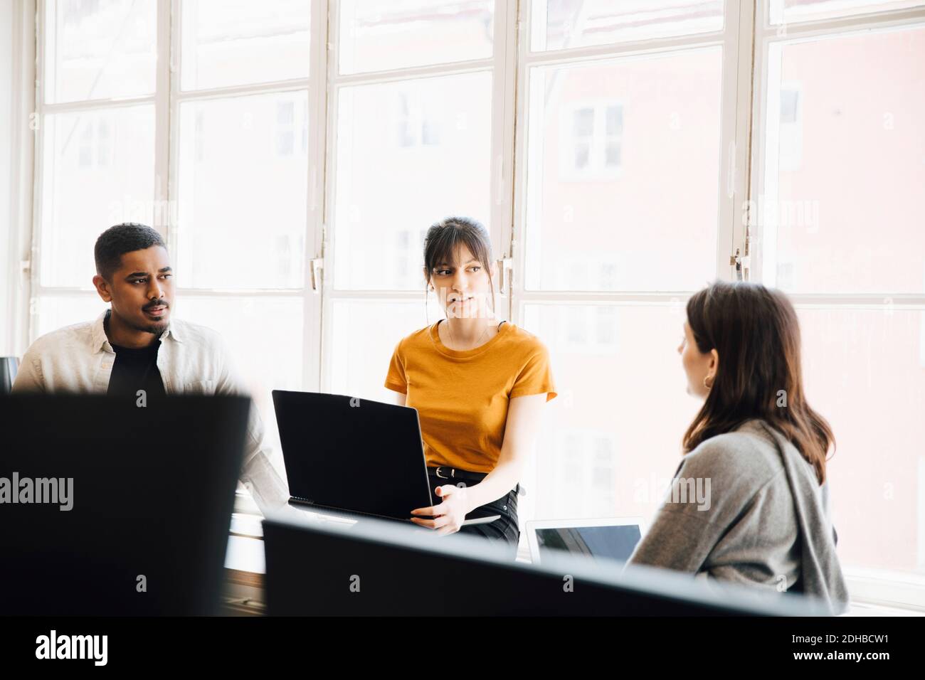 Eine Software-Ingenieurin erklärt den Mitarbeitern, während sie am Fenster sitzt Im Büro Stockfoto